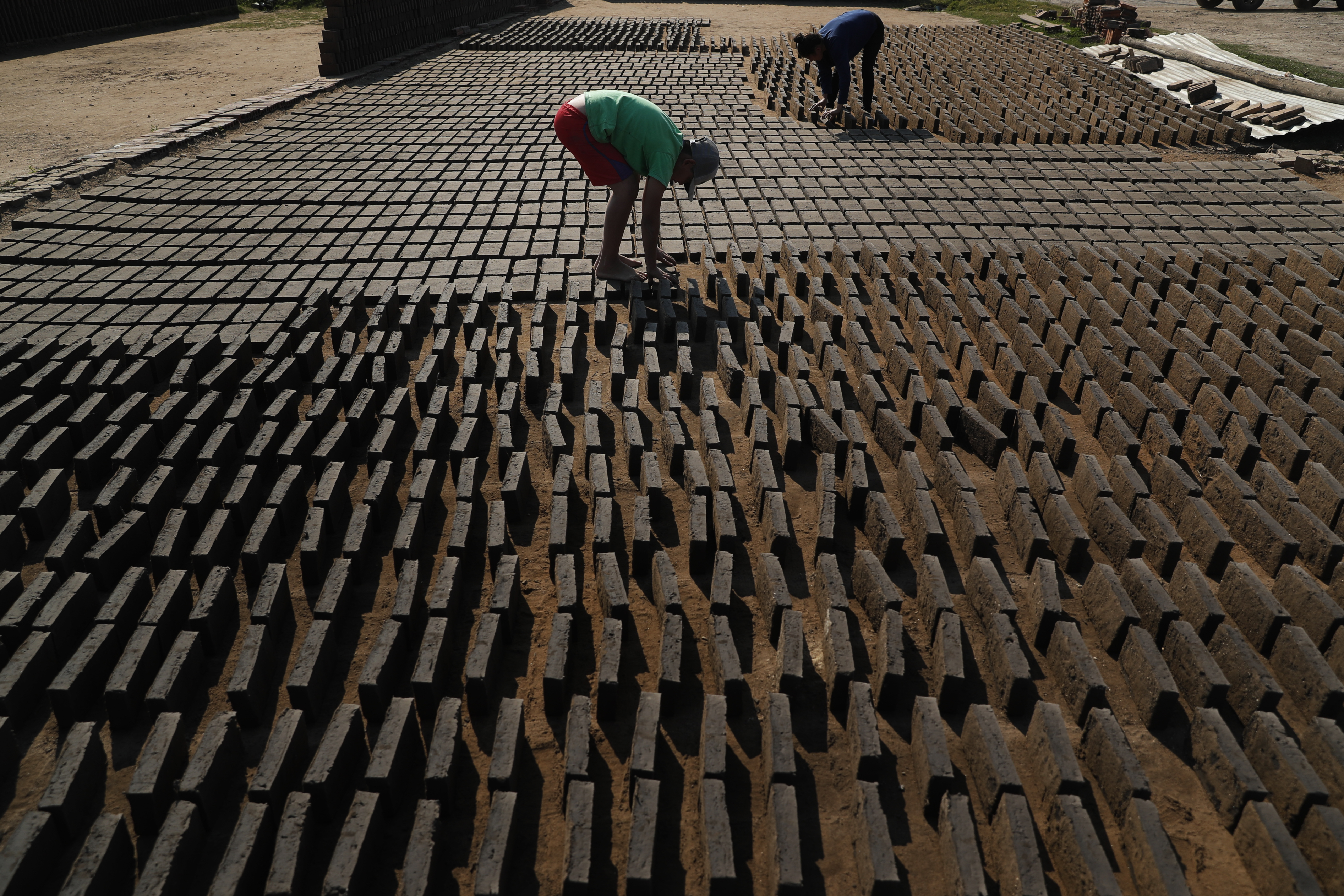 Cristian, en el centro, voltea ladrillos de arcilla de lado mientras se secan al sol antes de colocarlos en un horno en una pequeña fábrica de ladrillos en Tobati, Paraguay, el lunes 24 de agosto de 2020.