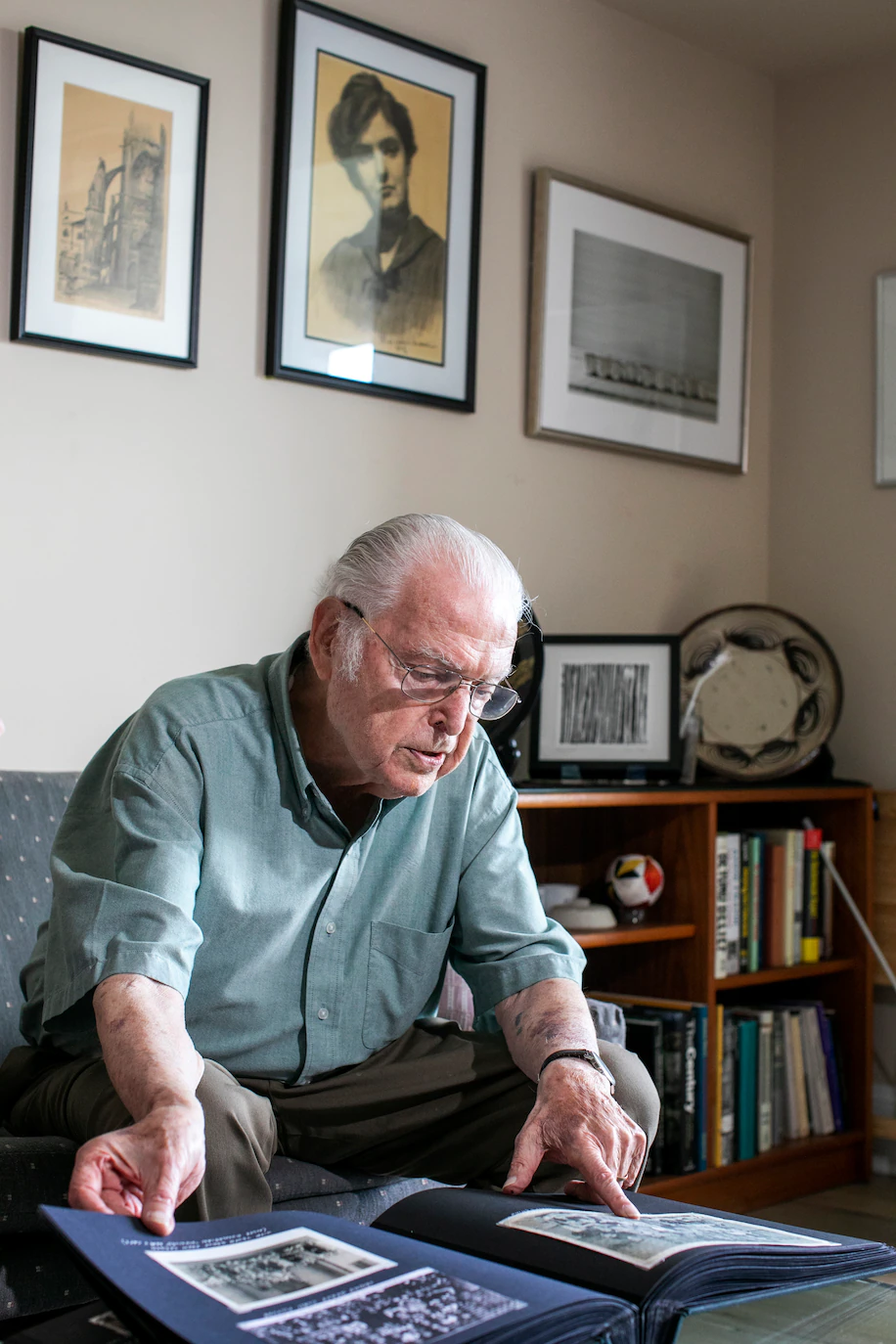 El sobreviviente del Holocausto Steven Fenves, de 91 años, mira un álbum de fotos familiar, debajo de un retrato de su madre y litografías de ella. (Deb Lindsey para The Washington Post)