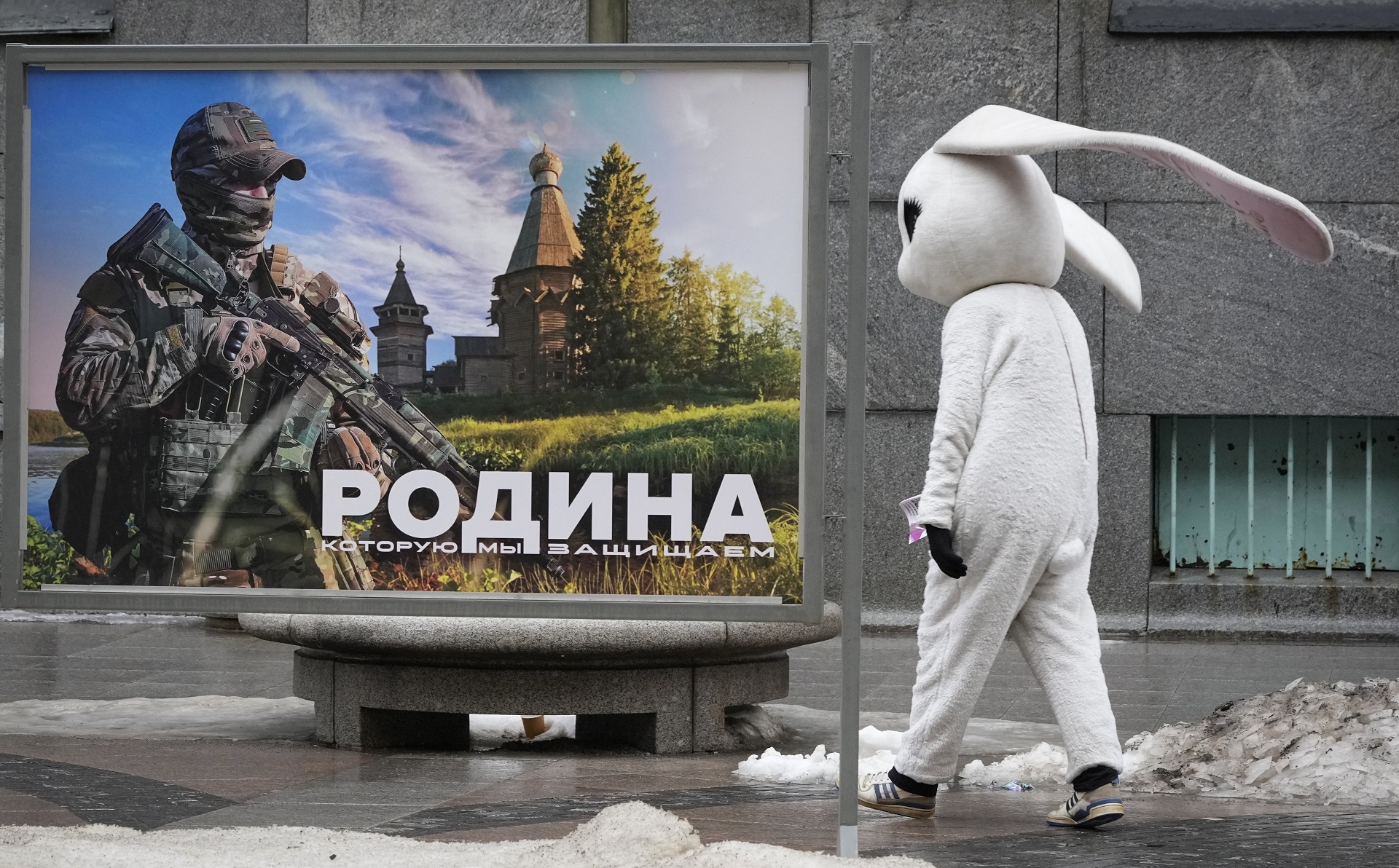 Una persona disfrazada camina por un cartel que dice "La patria que defendemos" en San Petersburgo (AP)