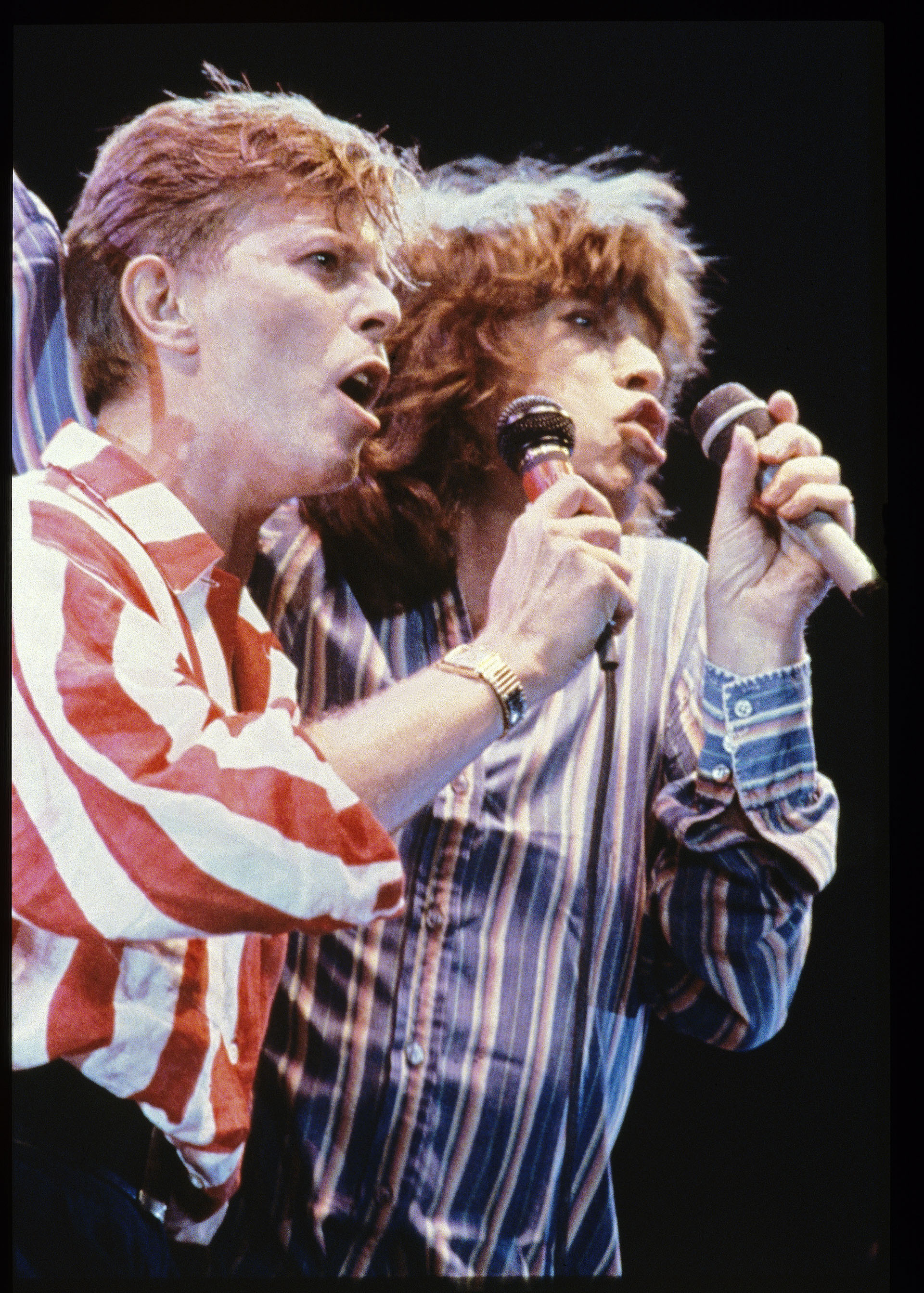 David Bowie y Mick Jagger a mediados de los ochenta cantando en un concierto benéfico. La ex esposa de Mick en sus memorias contó que una tarde los encontró desnudos en la cama (Brian Cooke/Redferns) 