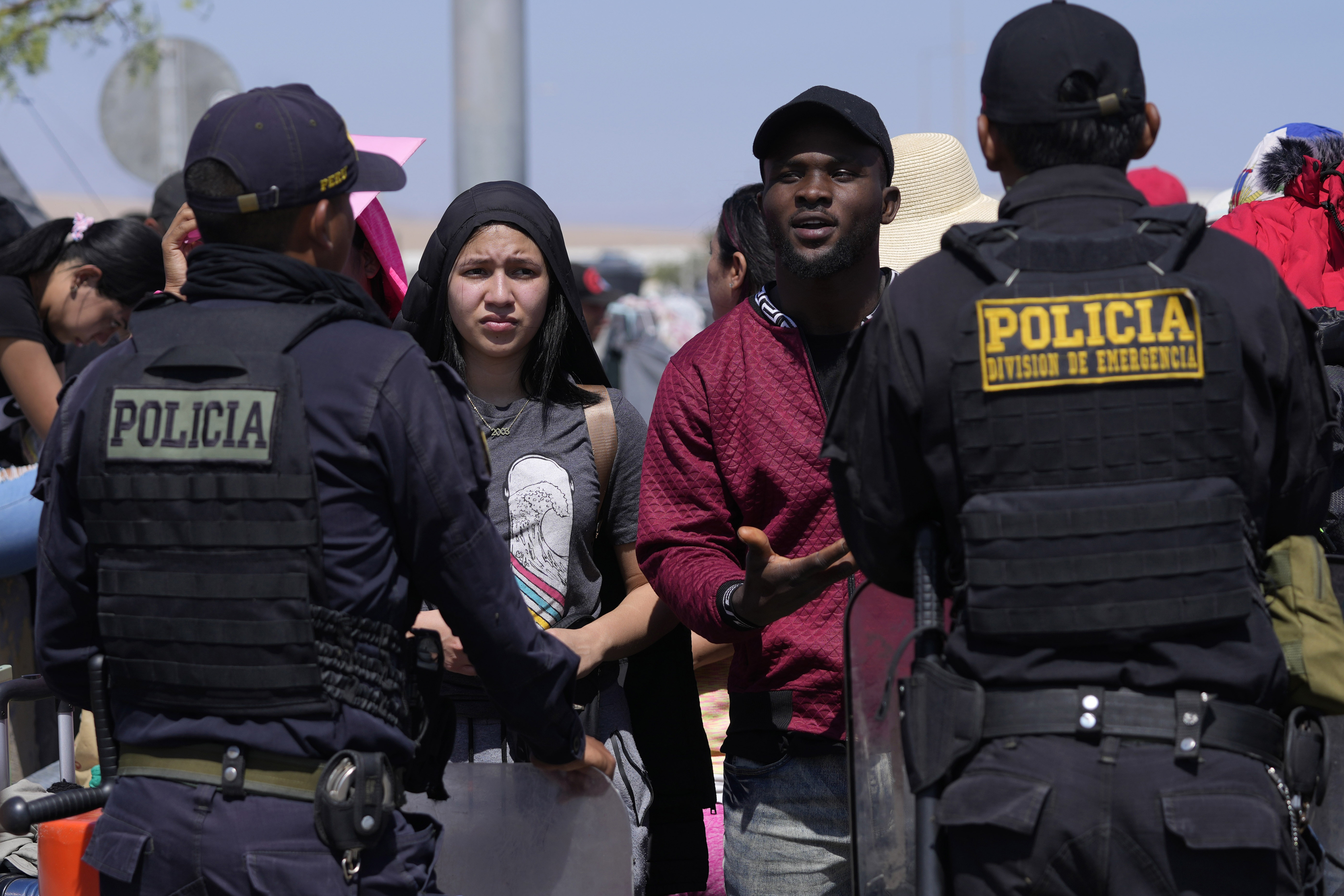 Venezuelan migrants talk with Peruvian police officers guarding the border with Chile, in Tacna, Peru, Friday, April 28, 2023. The migration crisis on the Chile-Peru border intensified on Thursday with hundreds of migrants left stranded. at the border limit, without being able to cross into Peru.  (AP Photo/Martín Mejía)