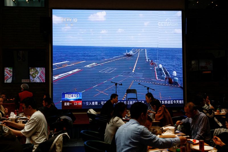 Clientes cenan en Beijing cerca de una pantalla gigante que emite imágenes de un avión que despega del portaaviones Shandong de China mientras participa en una patrulla de preparación para el combate y en los ejercicios "Espada Conjunta" alrededor de Taiwán (Reuters)
