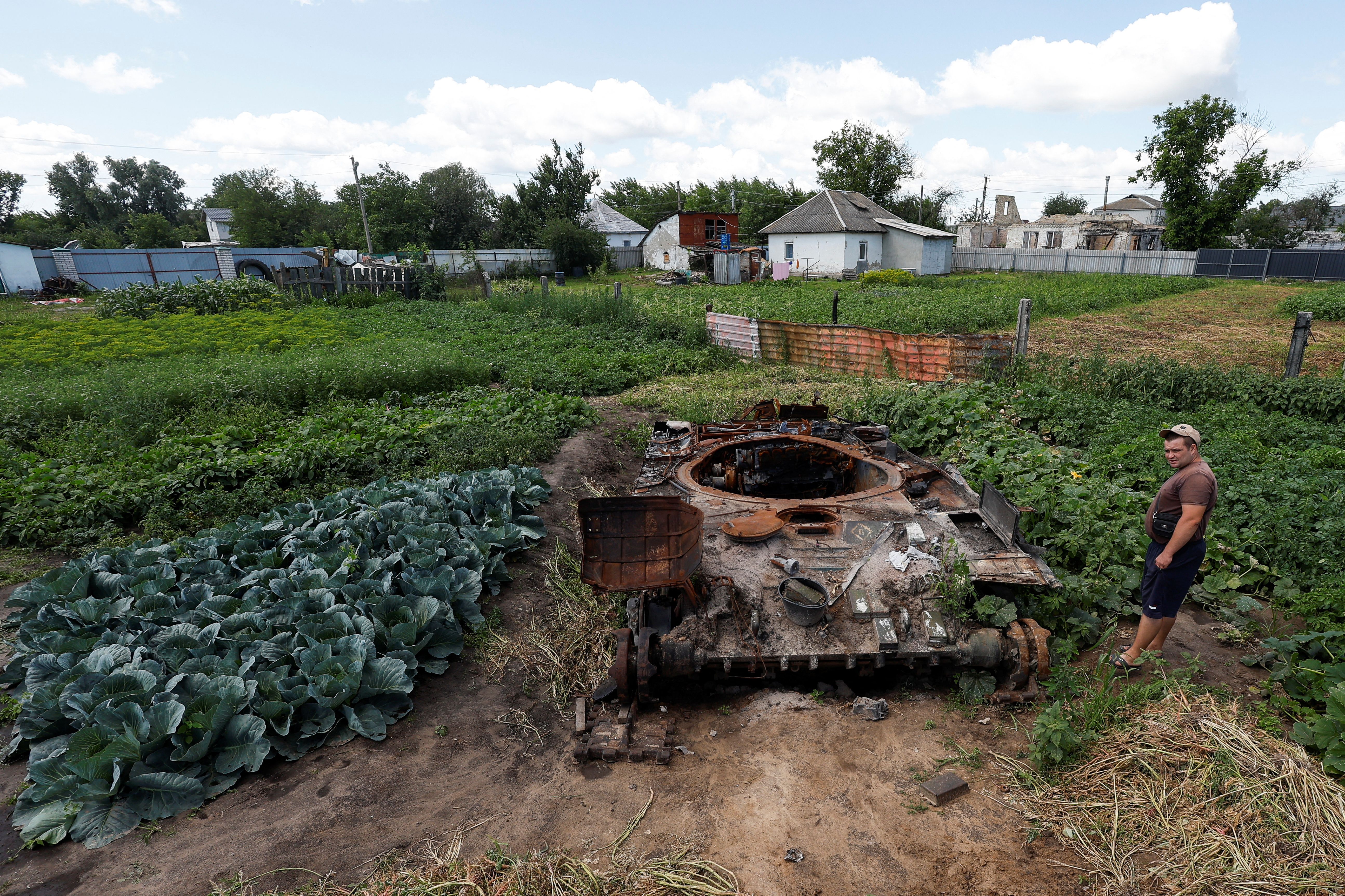 Un residente local se encuentra en el jardín de su casa cerca de un tanque ruso, destruido durante el ataque de Rusia a Ucrania, en la aldea de Velyka Dymerka, región de Kyiv (Reuters)