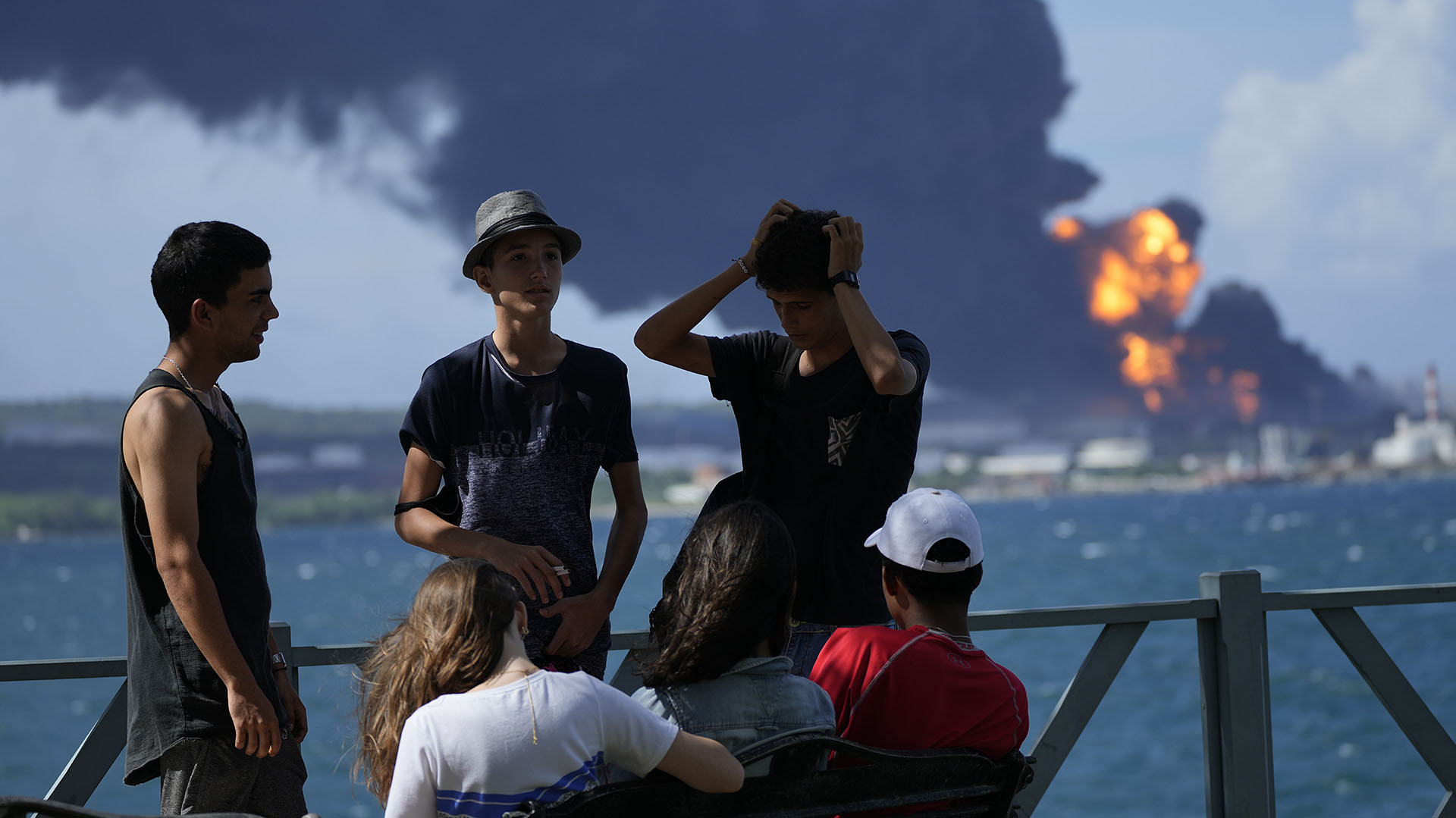 Jóvenes se reúnen en un muelle mientras las llamas y el humo siguen saliendo de la Base petrolera de Matanzas (AP/Ramon Espinosa)