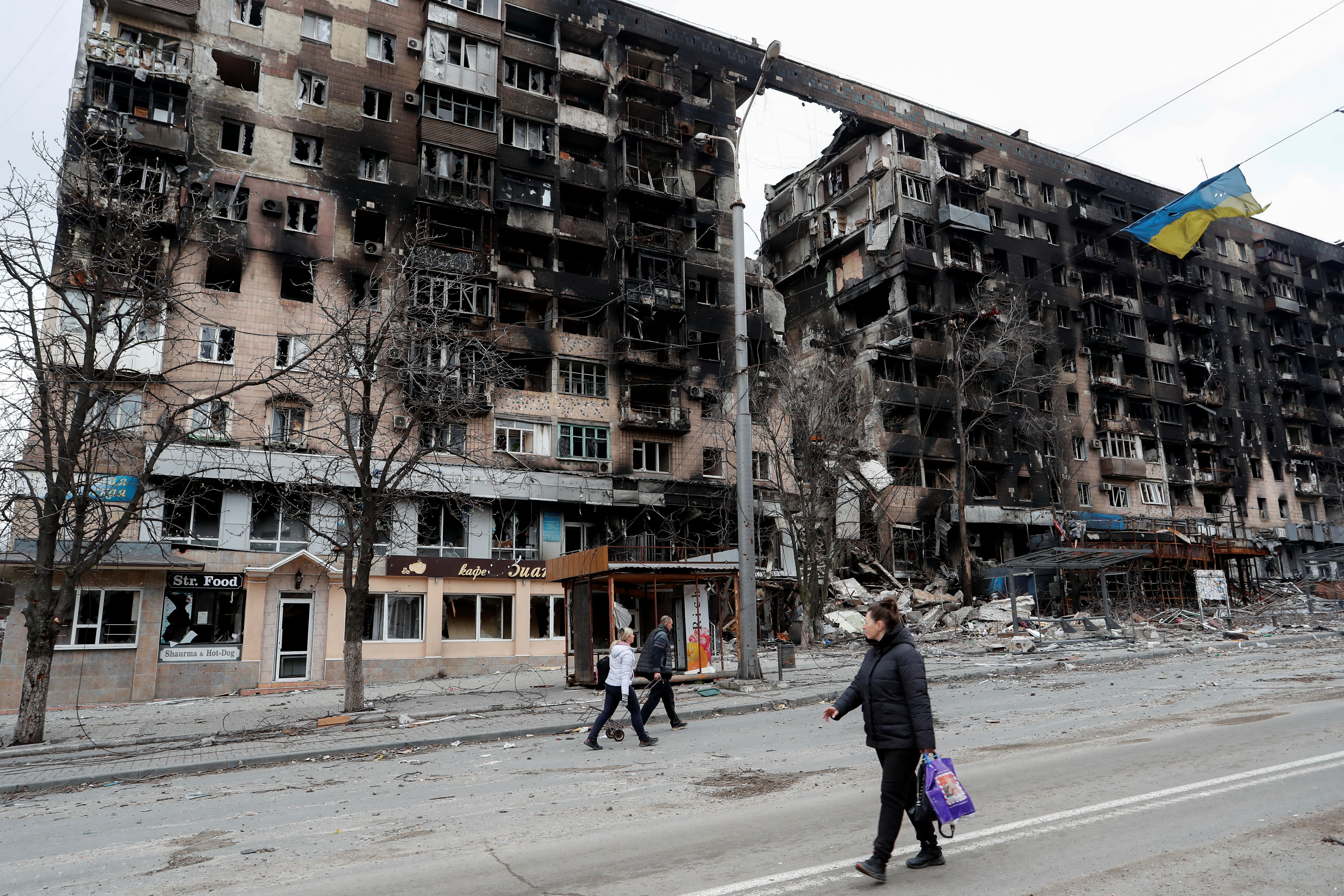 People walk along a street near a destroyed building in Mariupol