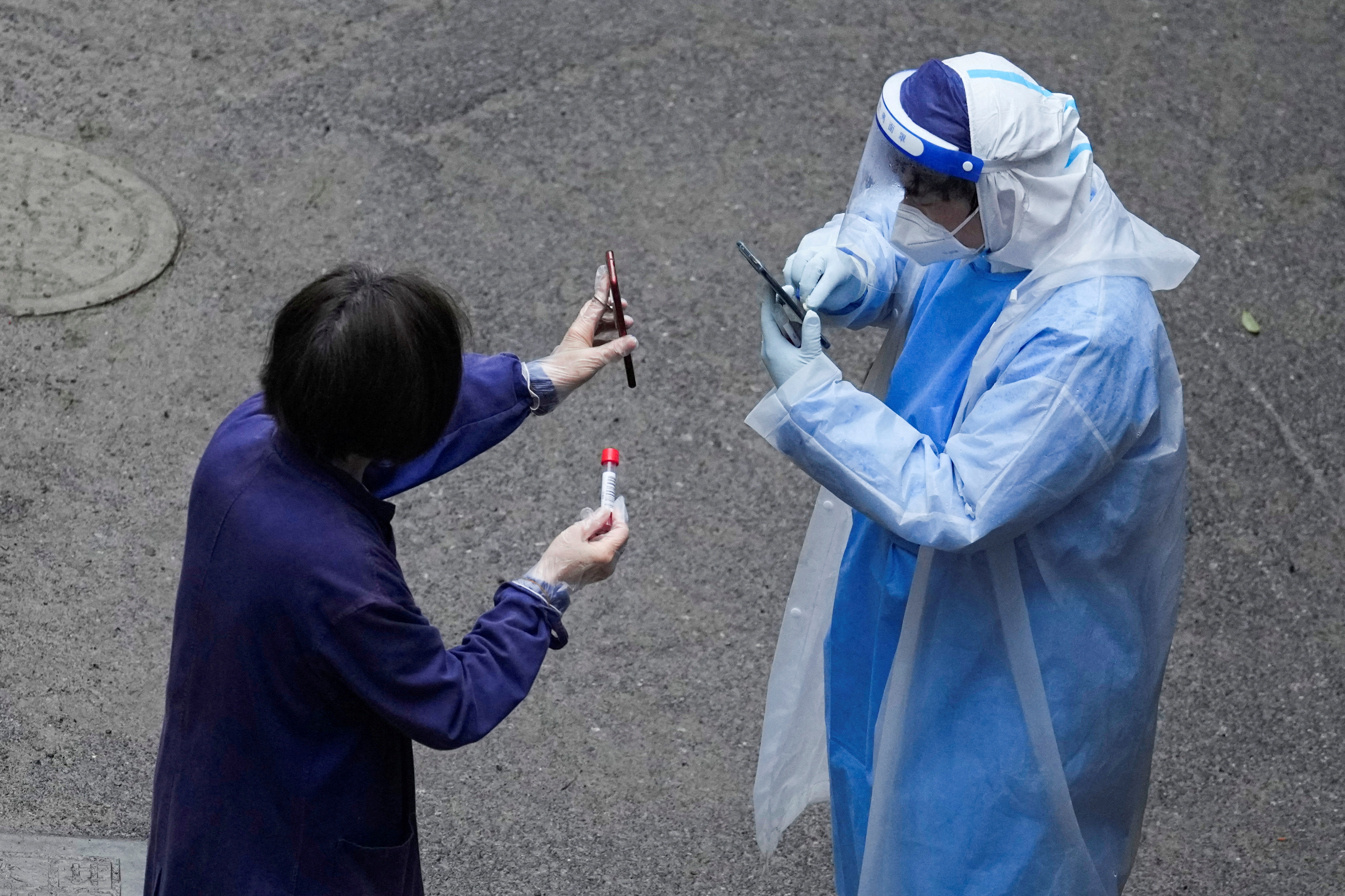 Un trabajador con traje protector verifica el código QR en el teléfono de un residente para realizar pruebas de ácido nucleico durante el encierro, en medio de la pandemia de la enfermedad por coronavirus (COVID-19), en Shanghái, China