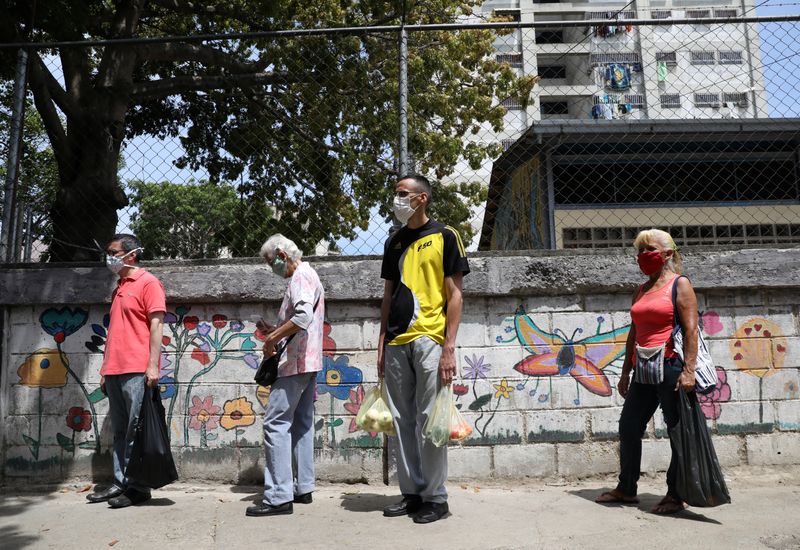 Gente con mascarillas hace una fila para comprar vegetales en un mercado callejero, durante la cuarentena nacional por el brote de coronavirus en Caracas (Reuters)