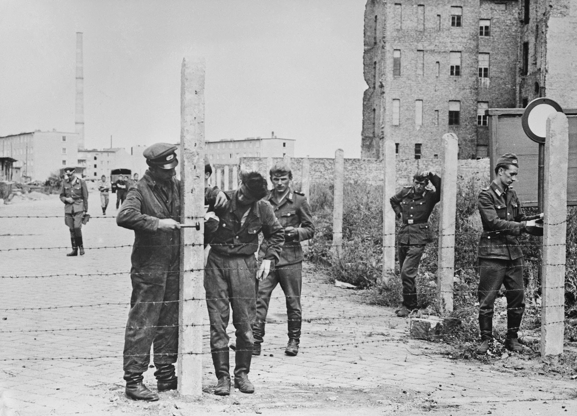 Soldados del Ejército Popular Nacional de Alemania Oriental (NVA) ponen alambradas para cerrar una calle en preparación para la construcción del Muro de Berlín, el 14 de agosto de 1961. Los primeros emplazamientos de hormigón fueron erigidos tres días después, el 17 de agosto (Keystone/Hulton Archive/Getty Images) 