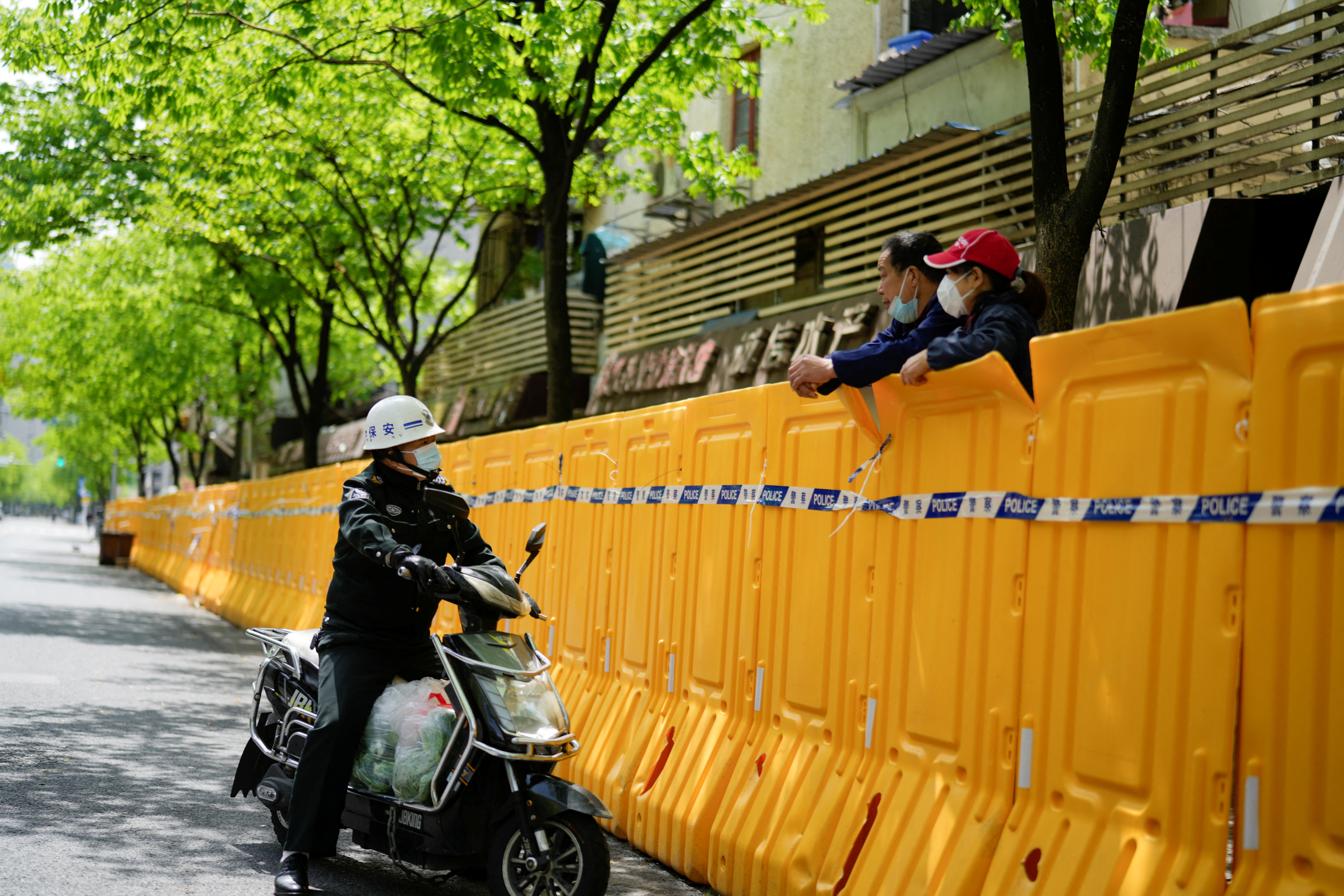 Un guardia de seguridad trata de conseguir comida hablando con un vendedor detrás de una área sellada por el confinamiento en Shanghai, China (REUTERS/Aly Song)