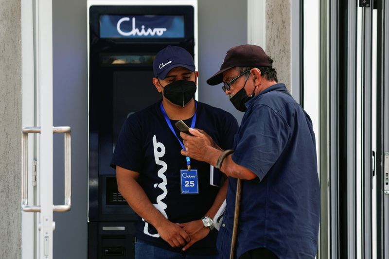 Un trabajador ayuda a un hombre con el uso de bitcoin frente a un cajero automatica de "Chibo", la billetera digital respaldada por el gobierno salvadoreño, en San Salvador, El Salvador. 8 September 2021.  (REUTERS/Jose Cabezas)