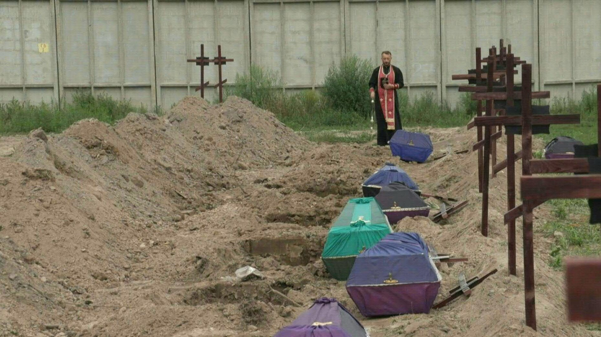 Recubiertos de un tejido color púrpura, once féretros alineados esperan sepultura, cada uno ante una tumba recién cavada en el cementerio de Bucha cerca de Kiev