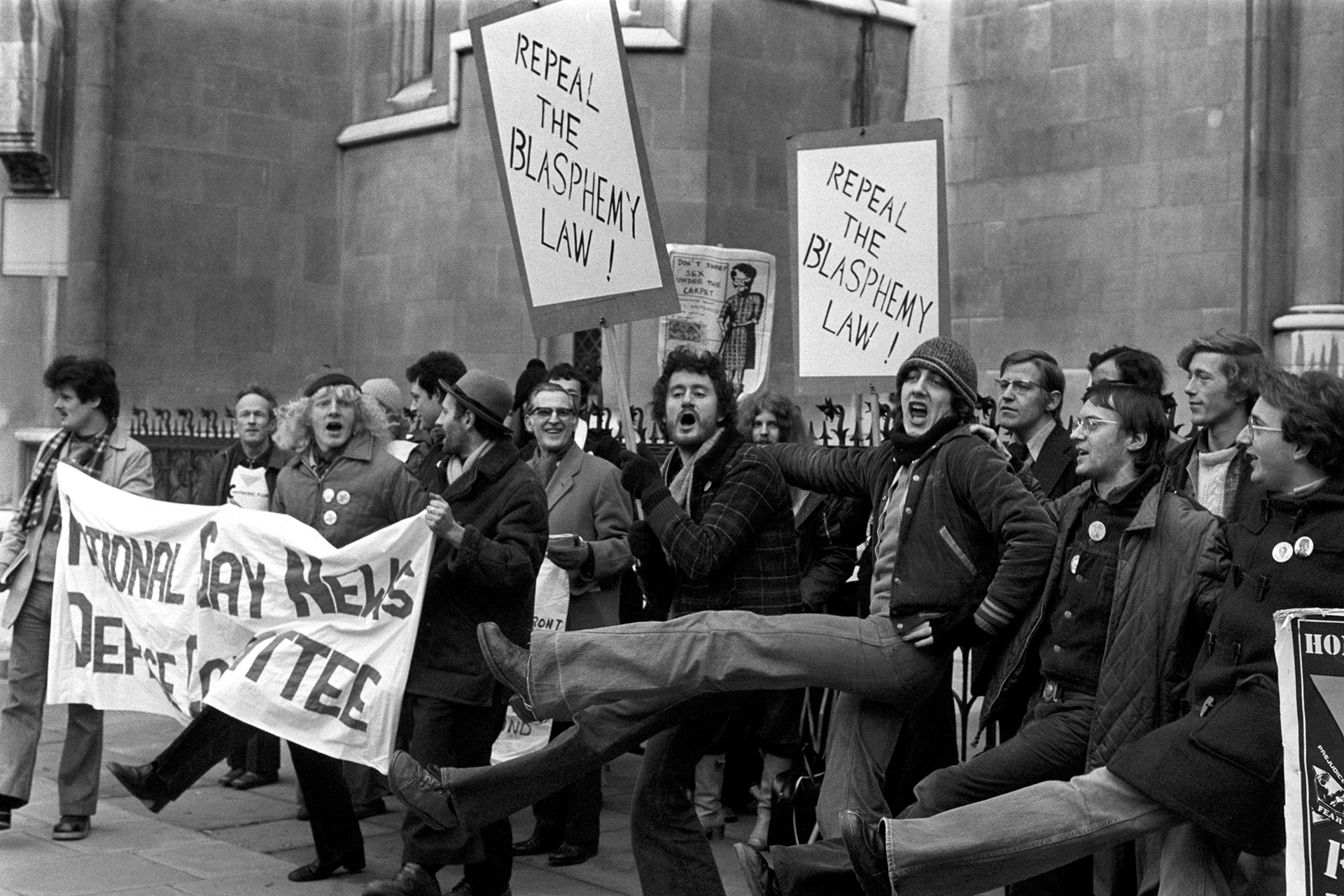 Patadas altas y pancartas desplegadas fuera de los Tribunales de Justicia, Strand, Londres, durante una manifestación de los partidarios del periódico Gay News en 1978.