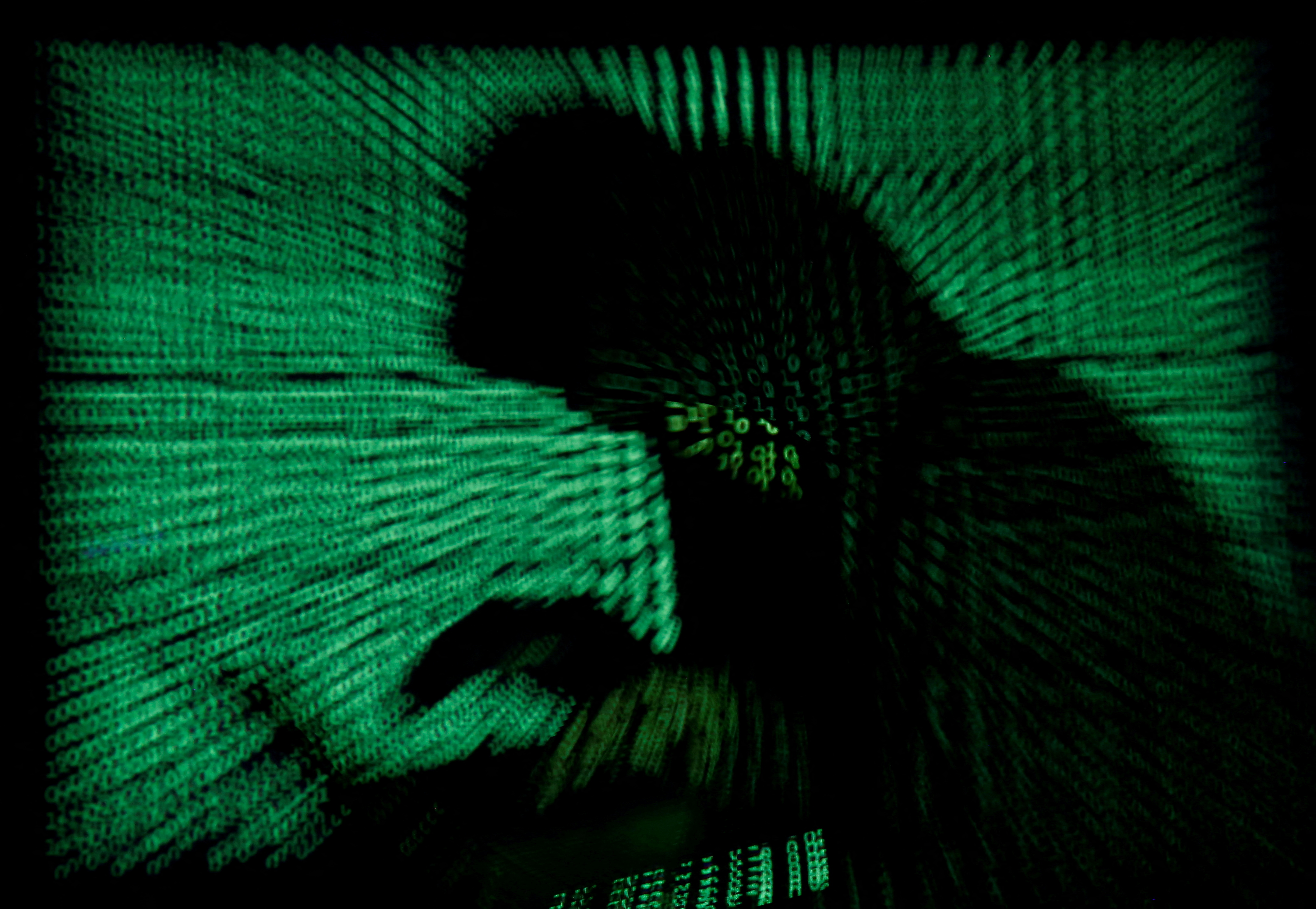 Un ciberdelincuente trabaja en su laptop mientras un complejo código se proyecta sobre su figura. Los piratas rusos continúan intentando penetrar las defensas ucranianas.  REUTERS/Kacper Pempel/Illustration.