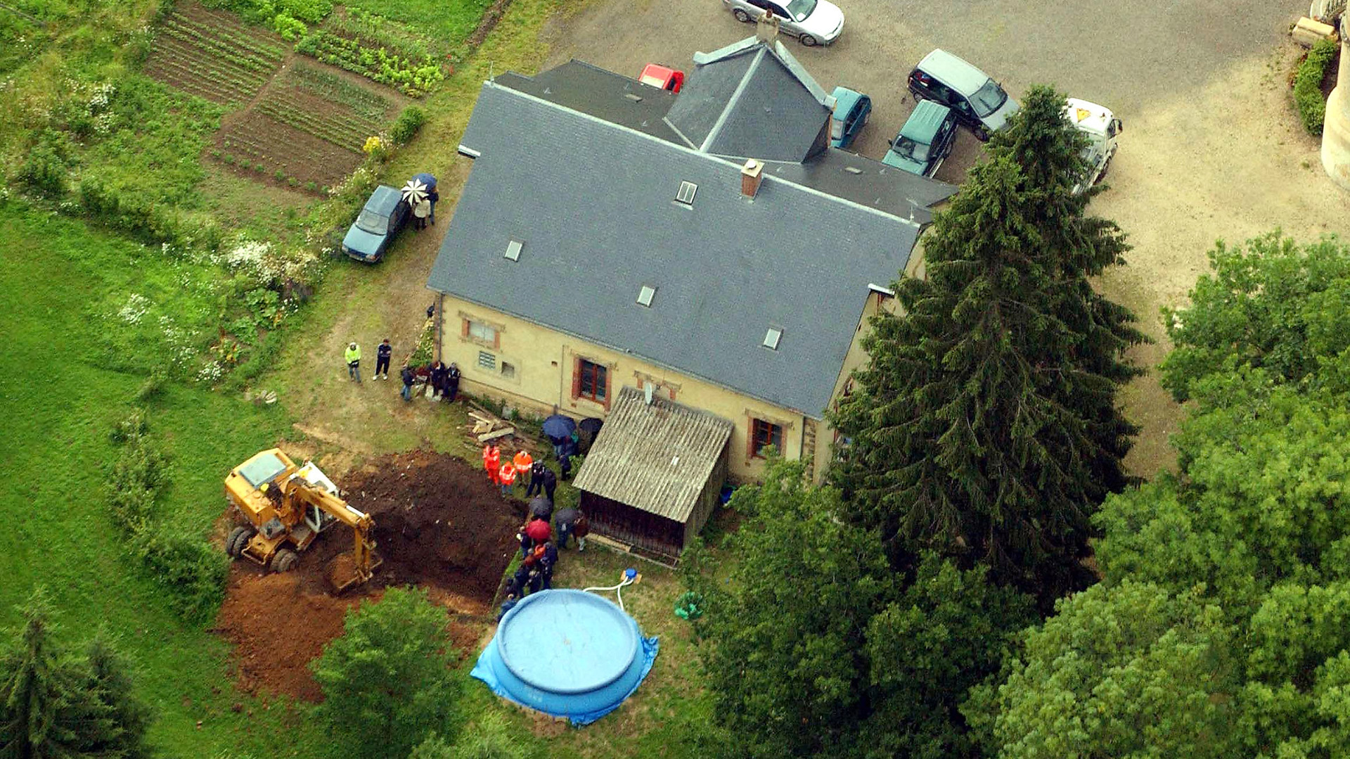 Vista aérea que muestra a los investigadores de la policía parados alrededor de una excavadora mecánica mientras buscan cuerpos en el parque del castillo 'Le Sautou' propiedad de Michel Fourniret cerca de Donchery, norte de Francia, 3 de julio de 2004. Fourniret confesó haber enterrado algunas de sus víctimas en este parque (Sylvain Lefevre/Getty Images)
