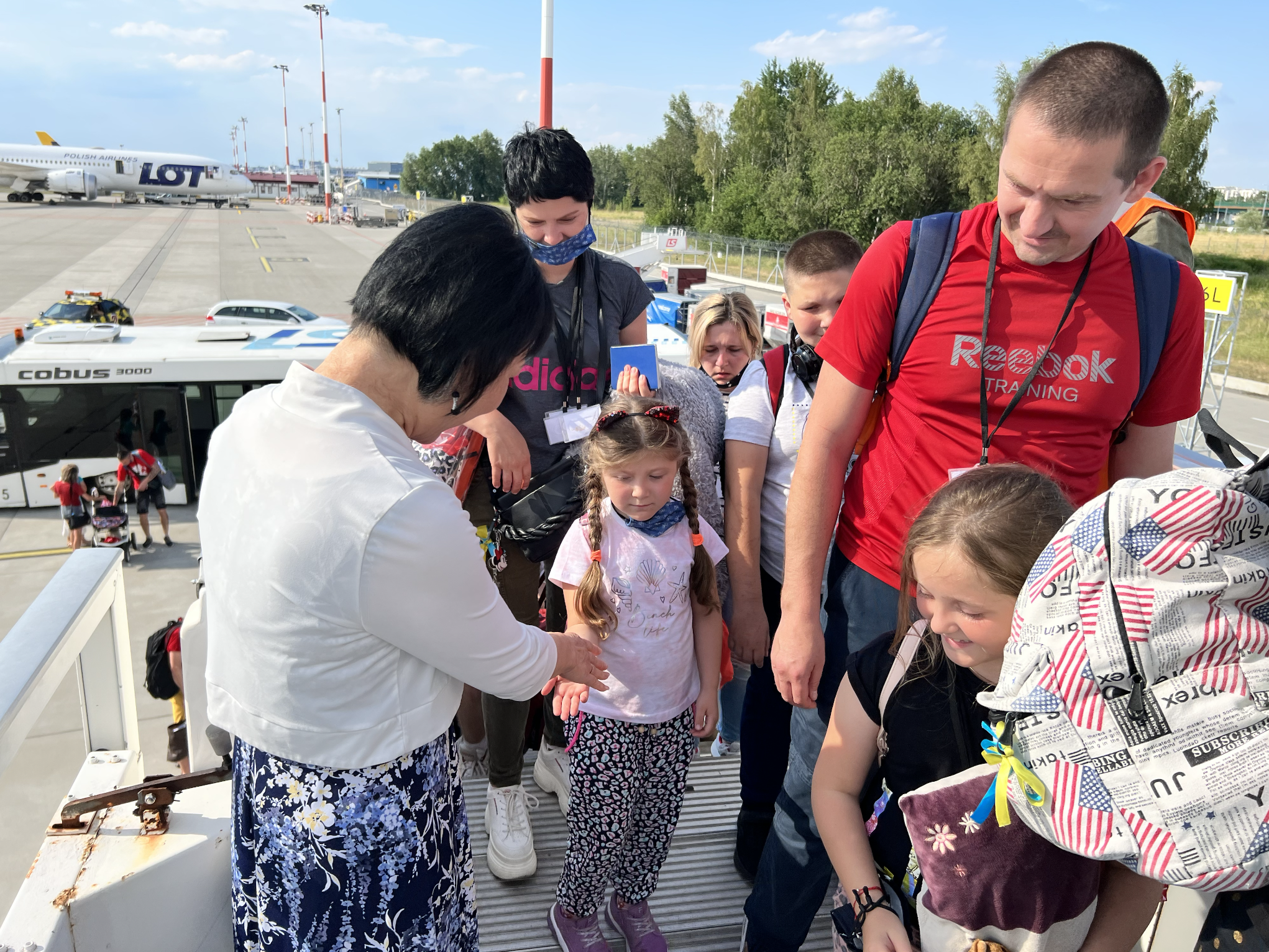Kim Phuc saluda a un grupo de niños ucranianos refugiados en el momento en que suben al avión de Enrique Piñeyro con rumbo a Canadá