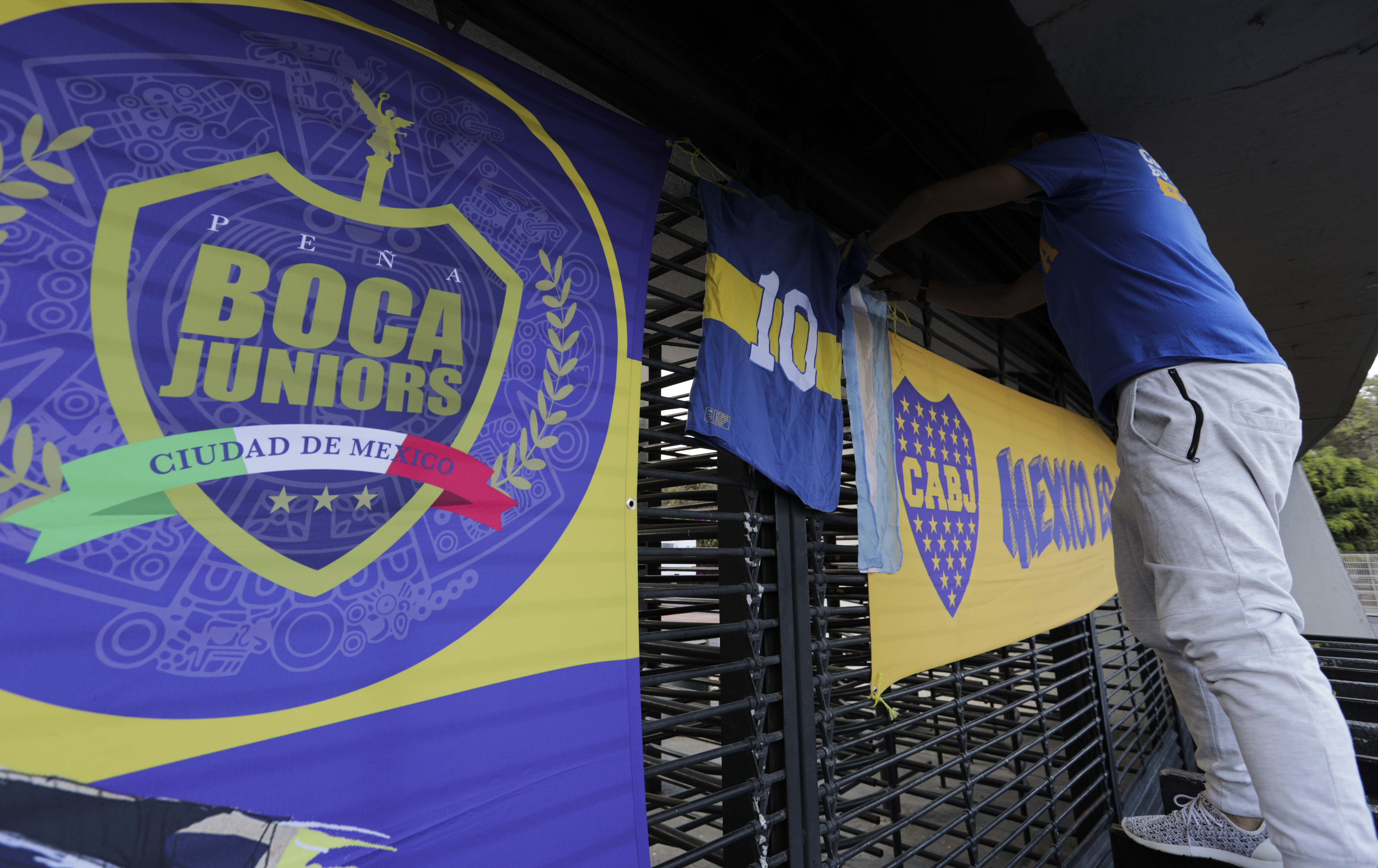 Un aficionado coloca una bandera argentina junto a las de Boca Juniors, en recuerdo de Diego Maradona, en la entrada del estadio Azteca de la Ciudad de México, el miércoles 25 de noviembre de 2020.