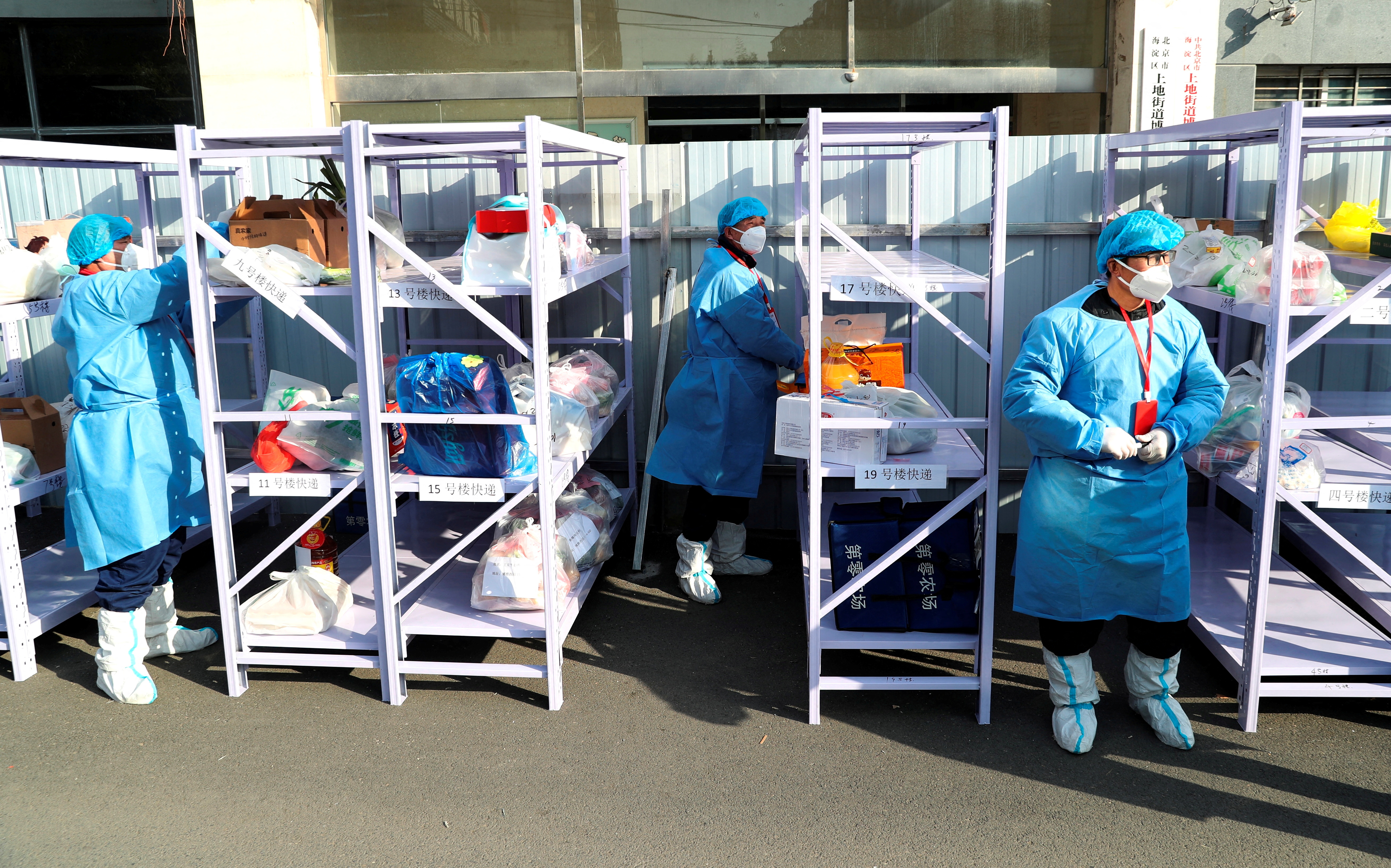 FILE PHOTO: Workers wearing protective suits following the coronavirus disease (COVID-19) outbreak stand next to daily necessities placed on makeshift delivery racks, at a residential compound under lockdown after a case of the Omicron variant was detected, in Beijing's Haidian district, China January 18, 2022. China Daily via REUTERS  ATTENTION EDITORS - THIS IMAGE WAS PROVIDED BY A THIRD PARTY. CHINA OUT./File Photo