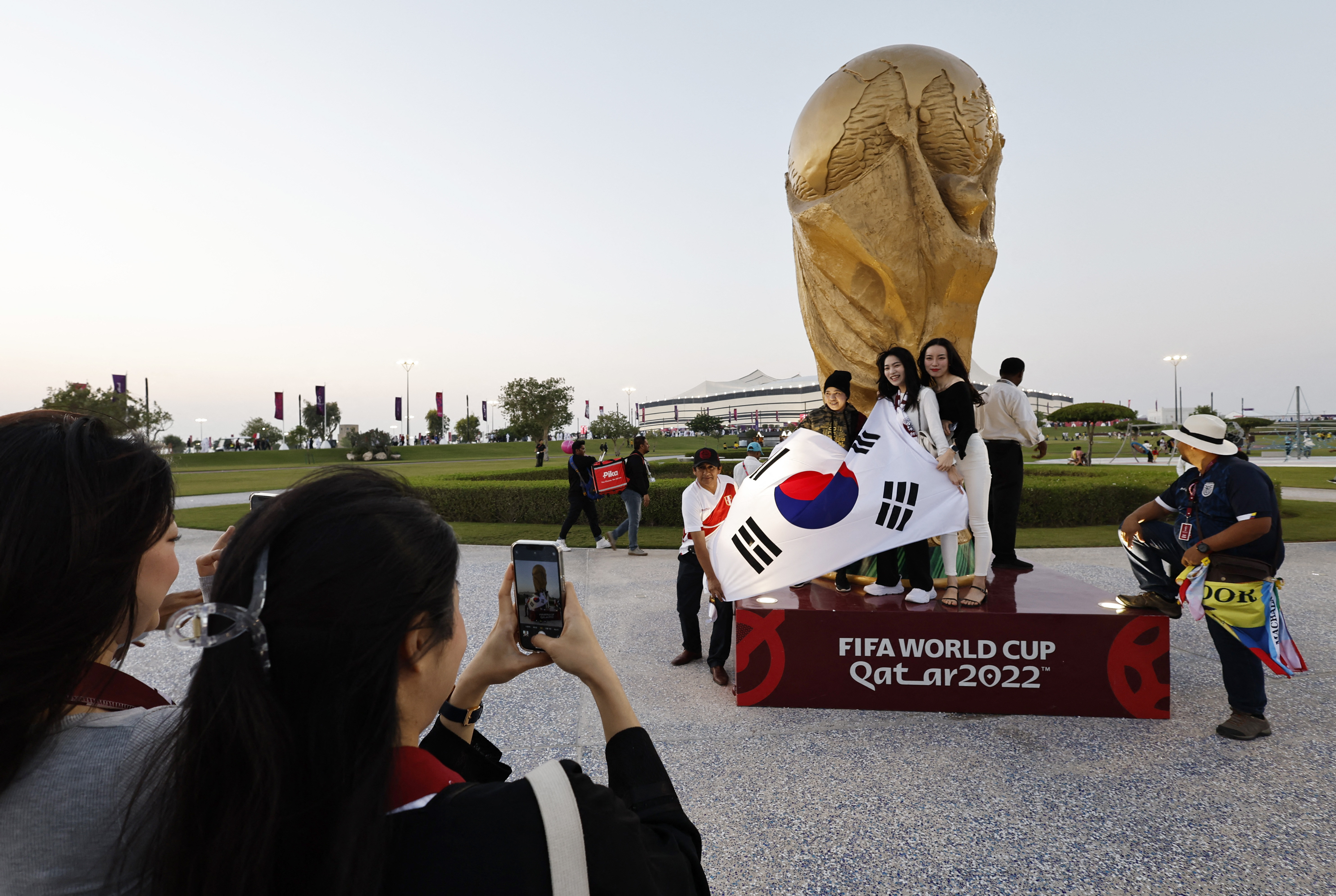Fanáticos con la bandera de Corea del Sur posan para una foto frente a una réplica de la Copa del Mundo fuera del estadio antes del partido. También hay un ecuatoriano y un peruano (REUTERS/Hamad I Mohammed)