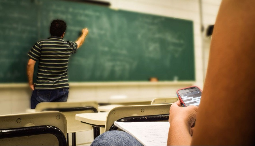 Un estudiante consulta su celular mientras el profesor da su clase.