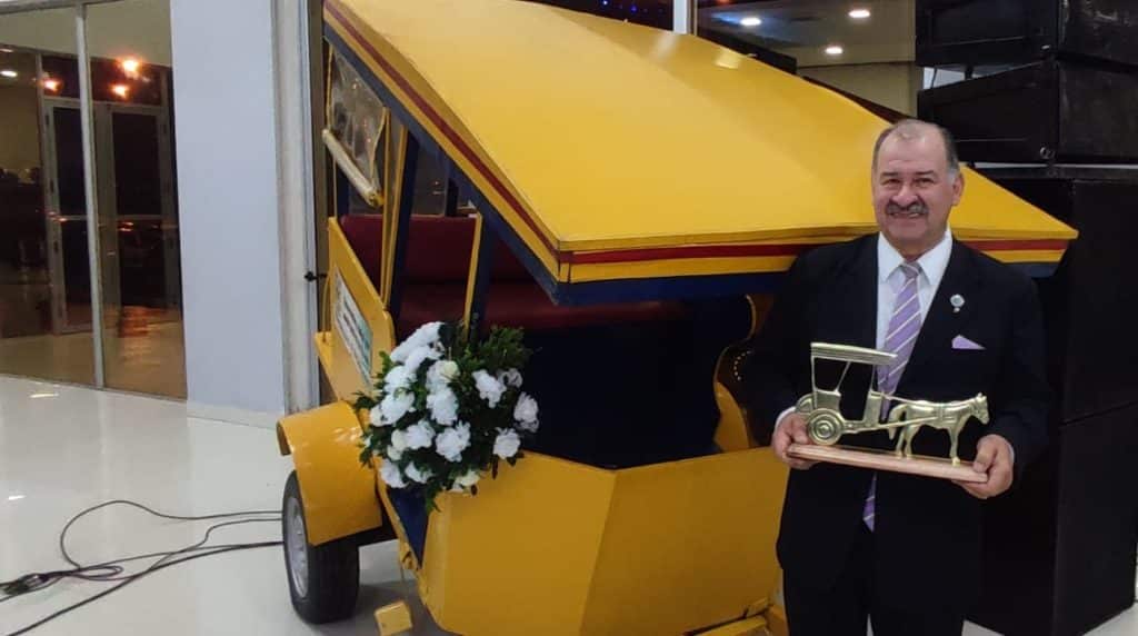 Nicolás Rey Martínez posa con la estatuilla del "Premio Karumbe" al lado del icónico medio de transporte de pasajeros tirado por caballos, el karumbe, hoy en día un patrimonio de la historia de la ciudad.
