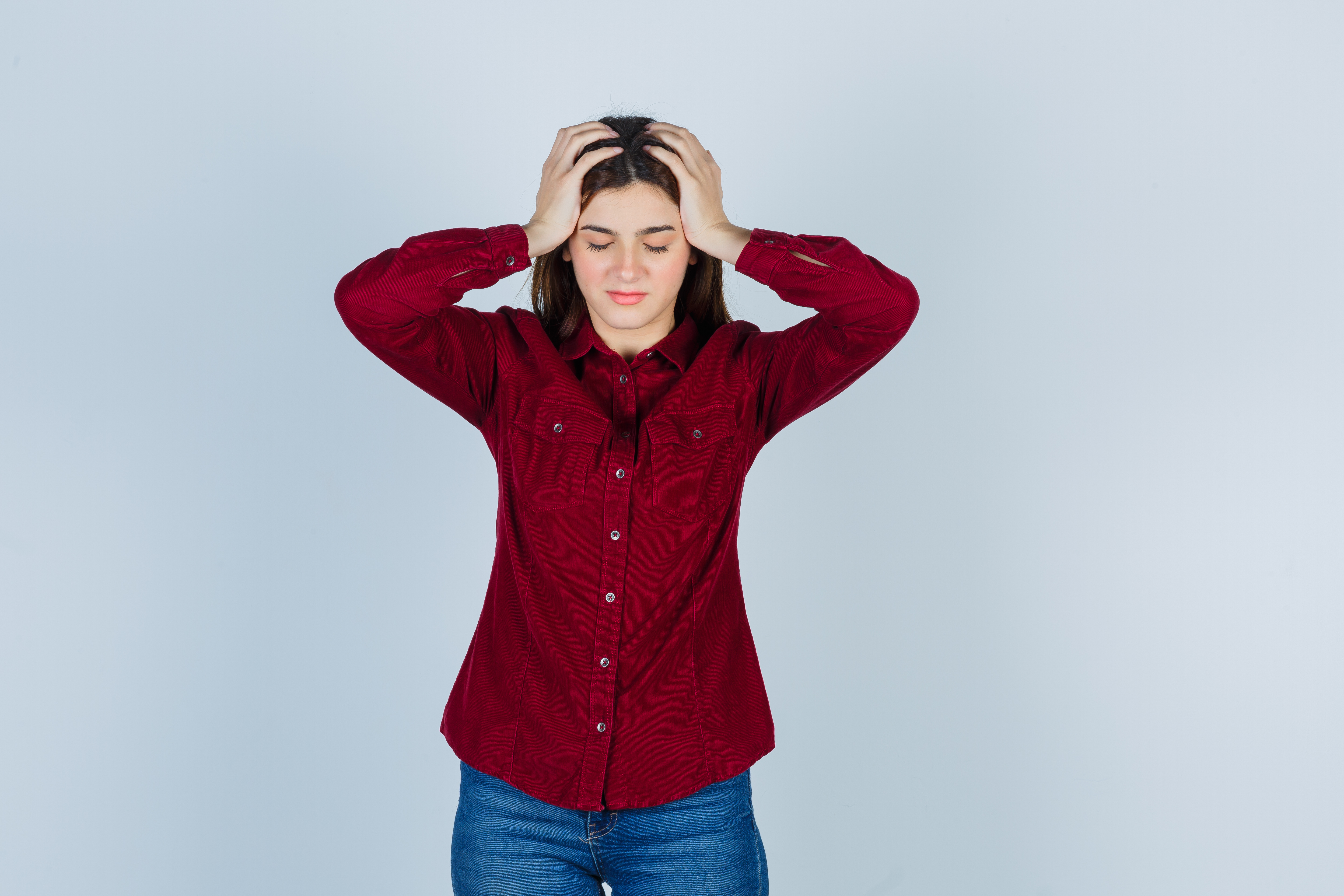teenage girl in casual shirt keeping hands on head, shutting eyes and looking depressed , front view.