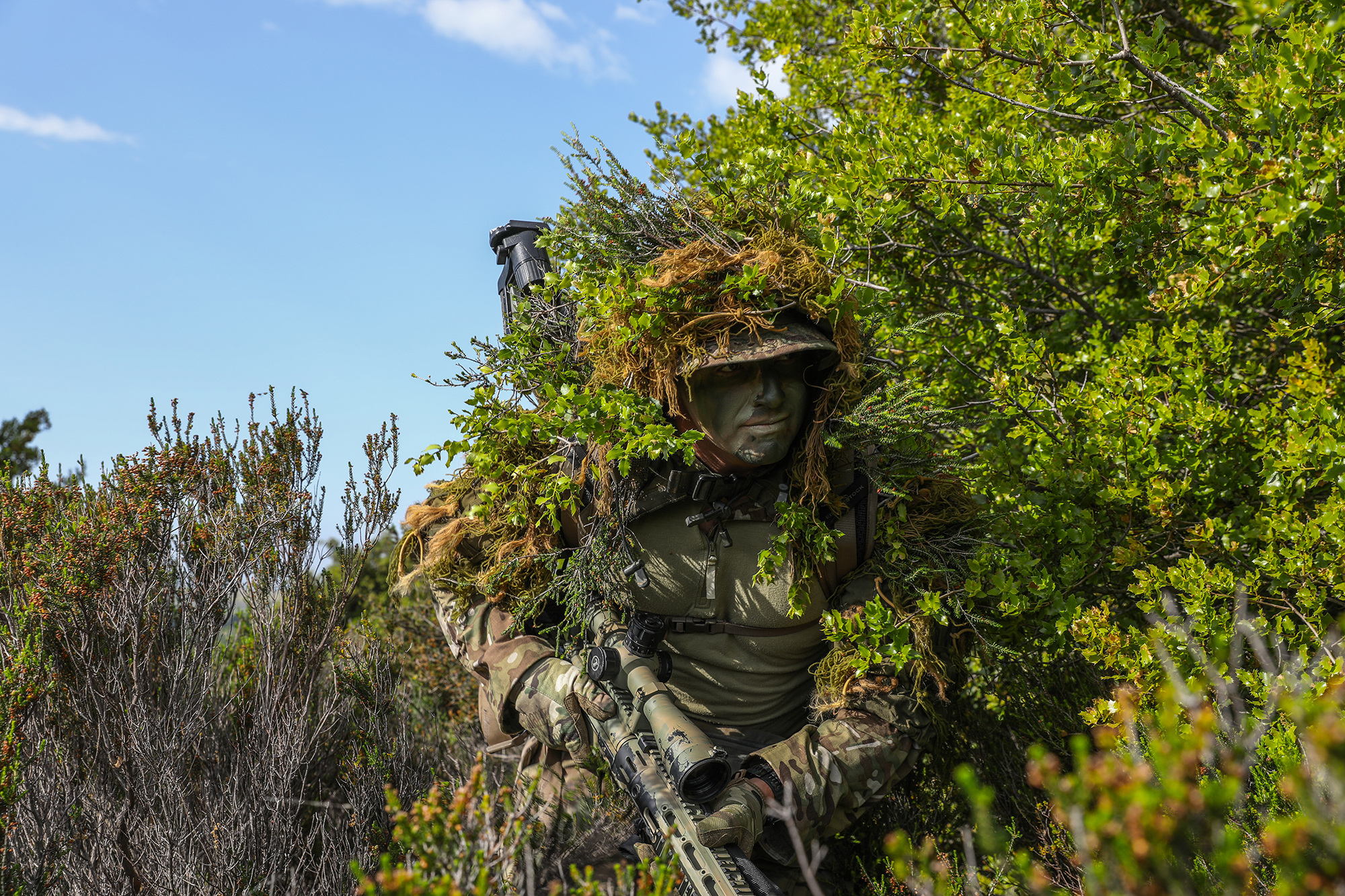 Alabama Army National Guardsman Spc. Dexter Hanson meshes his ghillie suit with the surrounding brush for better concealment during a training exercise in Xanthi, Greece, May 18, 2021. (Sgt. Samuel Hartley/Army)