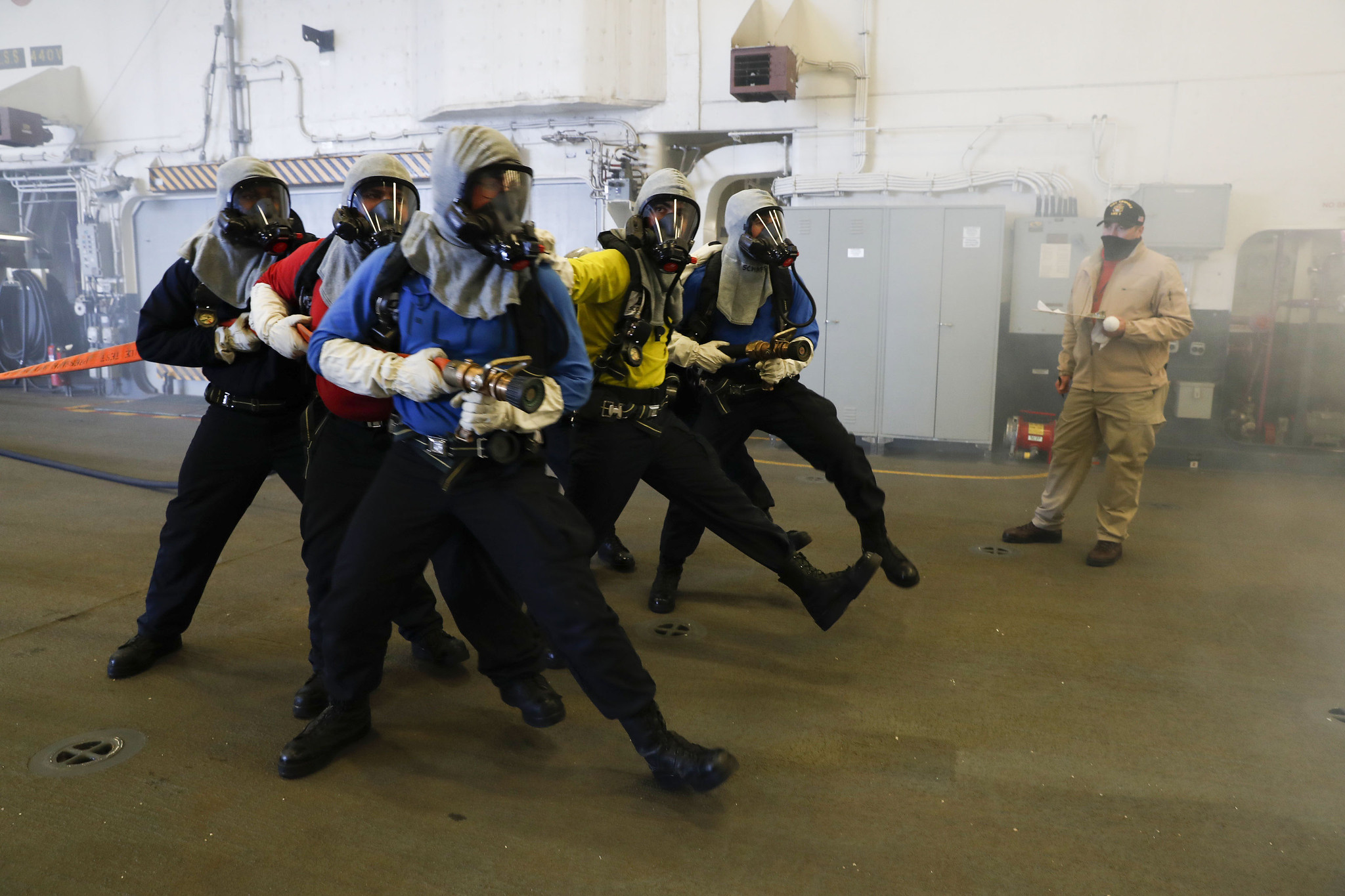 Aviation boatswain’s mates (handling) simulate approaching a fire during an aircraft firefighting drill in the hangar bay of the amphibious assault ship USS Tripoli (LHA 7), Aug. 31, 2020, in the Pacific Ocean. (MC1 Christopher B. Janik/Navy)
