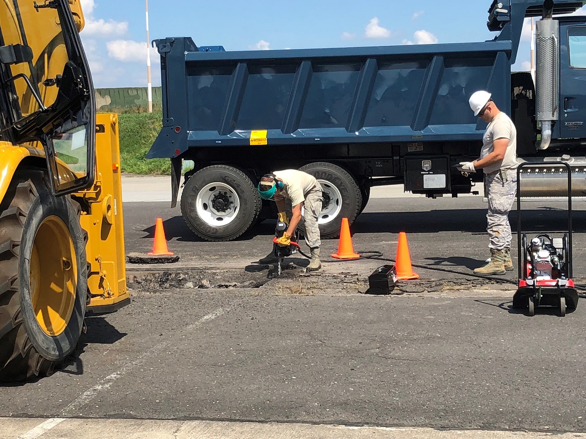 An airman uses a chainsaw to remove damaged concrete before a team of civil engineers fills a sinkhole on a maintenance apron on July 31 at the 31st Air Base near Krzesiny, Poland. (Valerie Insinna/Staff)