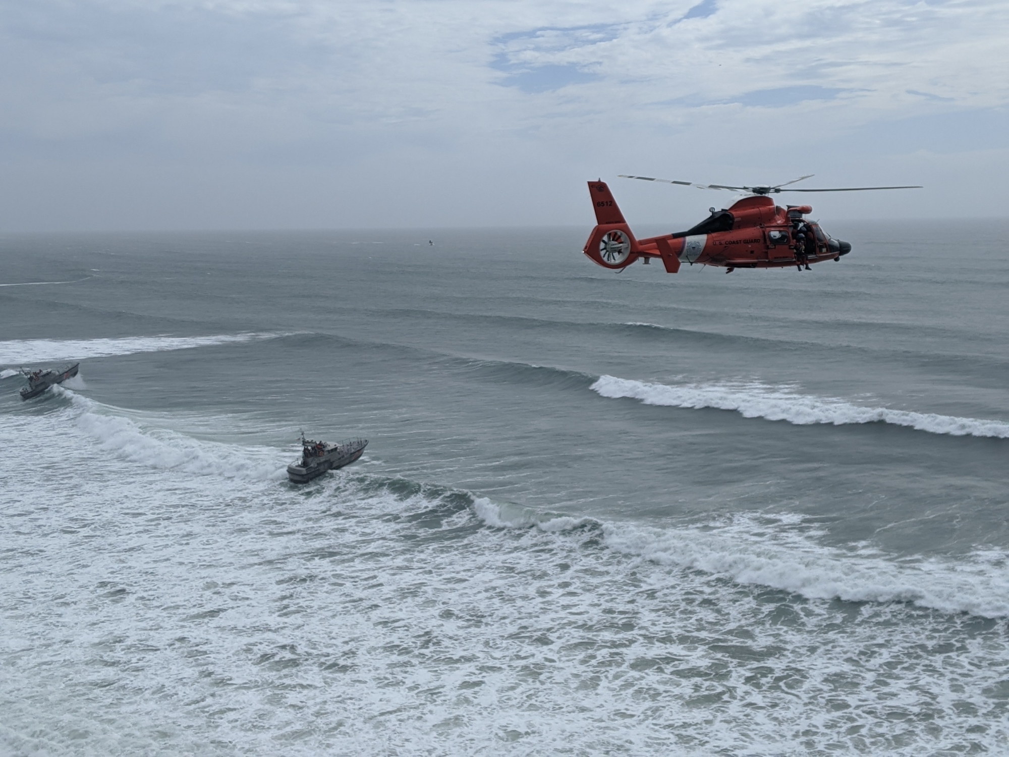An aircrew aboard an MH-65 Dolphin helicopter from Air Facility Newport arrives on scene during the rescue of seven people trapped on the cliffs near Yaquina Head, Ore., May 29, 2020. Two Station Yaquina Bay boatcrews aboard 47-foot Motor Lifeboats were positioned offshore as a contingency. (Petty Officer 2nd Class Michael Martini/Coast Guard)