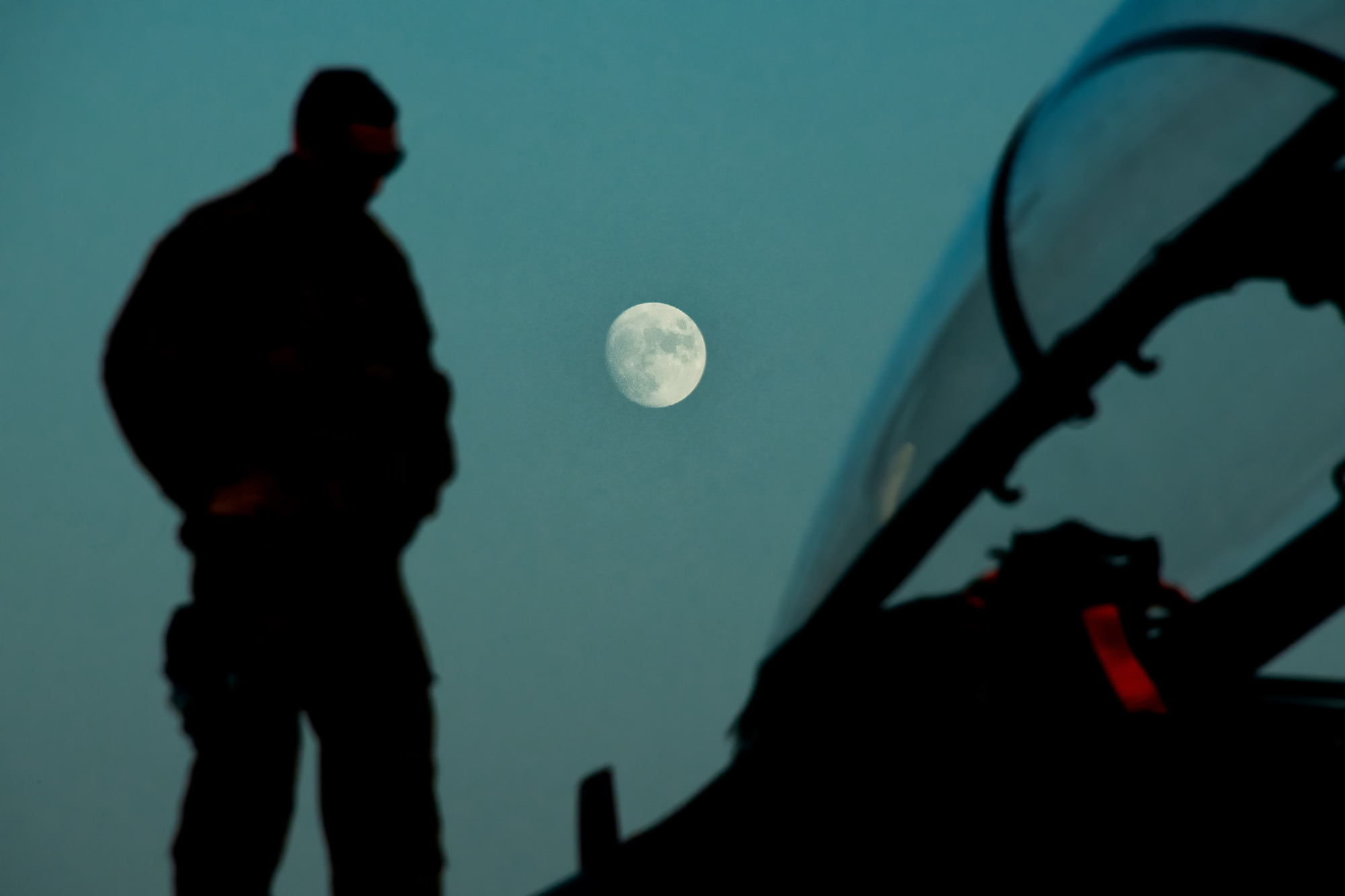 A maintainer deployed to the 332d Air Expeditionary Wing, checks an F-15E Strike Eagle during a routine post flight inspection Sept. 29, 2020, as the moon rises over the flightline in an undisclosed location. (Master Sgt. Jonathan Young/Air National Guard)