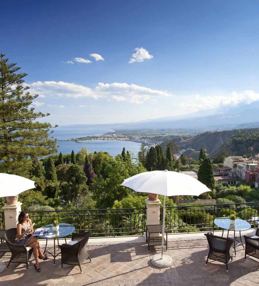 The neo-classical 1873 Belmond Grand Timeo. Its literary bar and terrace looks out over the Ionian Sea towards Calabria. Mount Etna is to the side and the bays of Mazzaro and Naxos below. The bar also has a third century amphitheatre in its back garden
