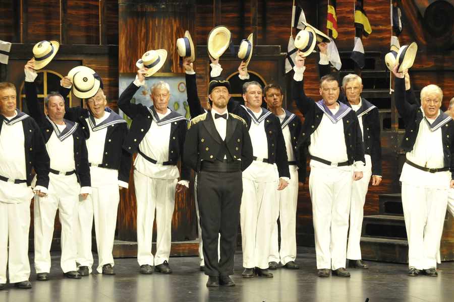 The chorus raise their hats during a scene from HMS Pinafore