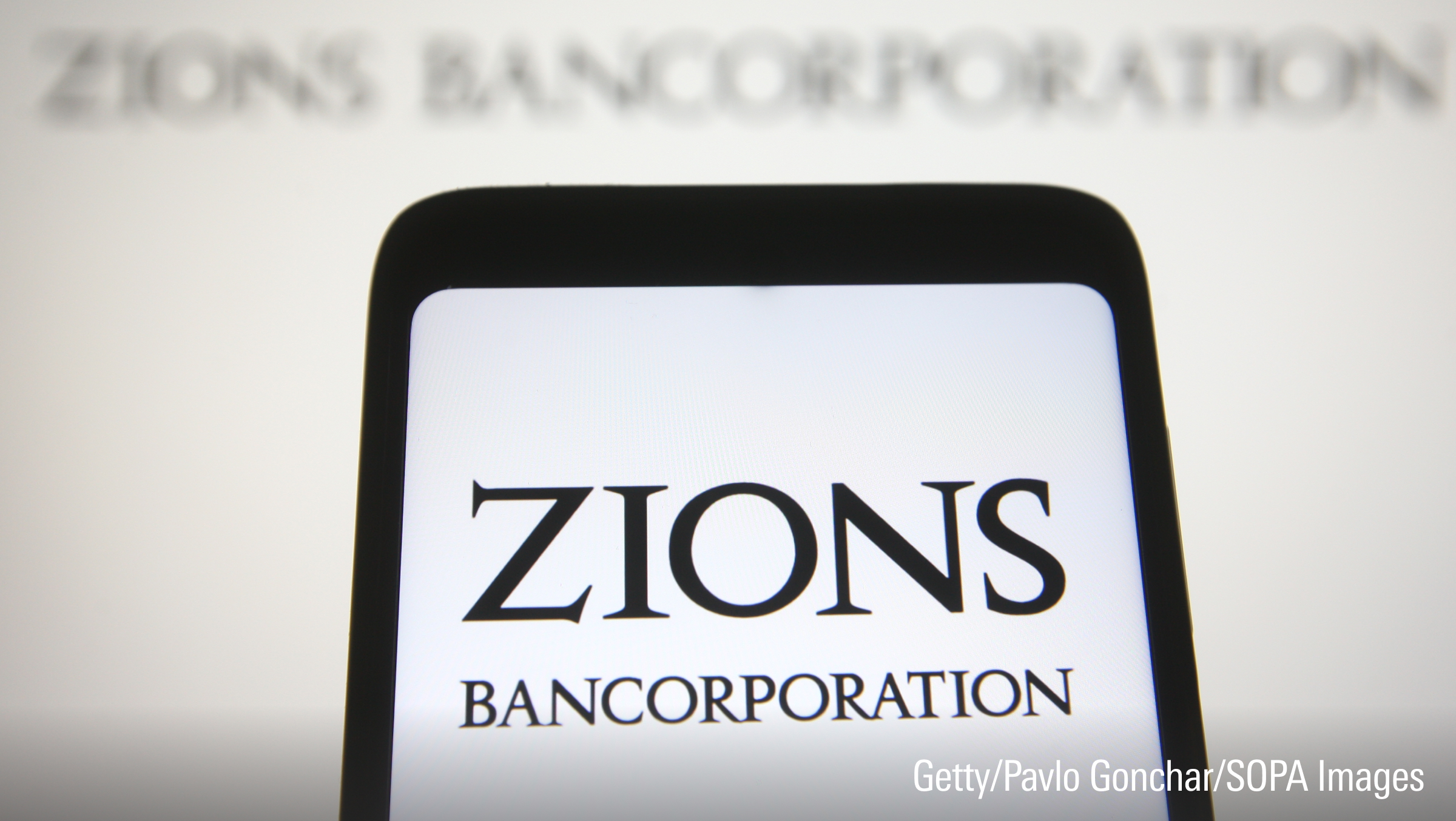 In this Photo illustration a Zions Bancorporation logo is seen on a smartphone and a pc screen.