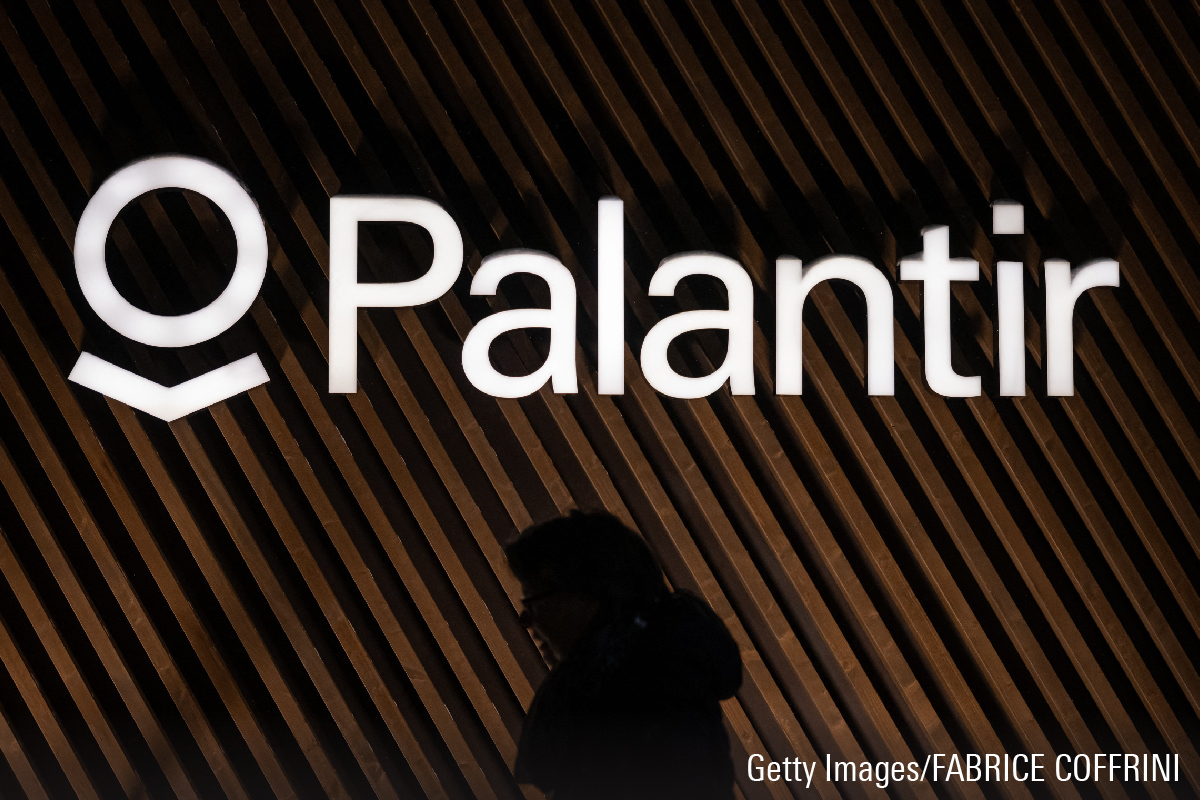This photograph shows a woman walking past the logo of Palantir Technologies during the World Economic Forum.