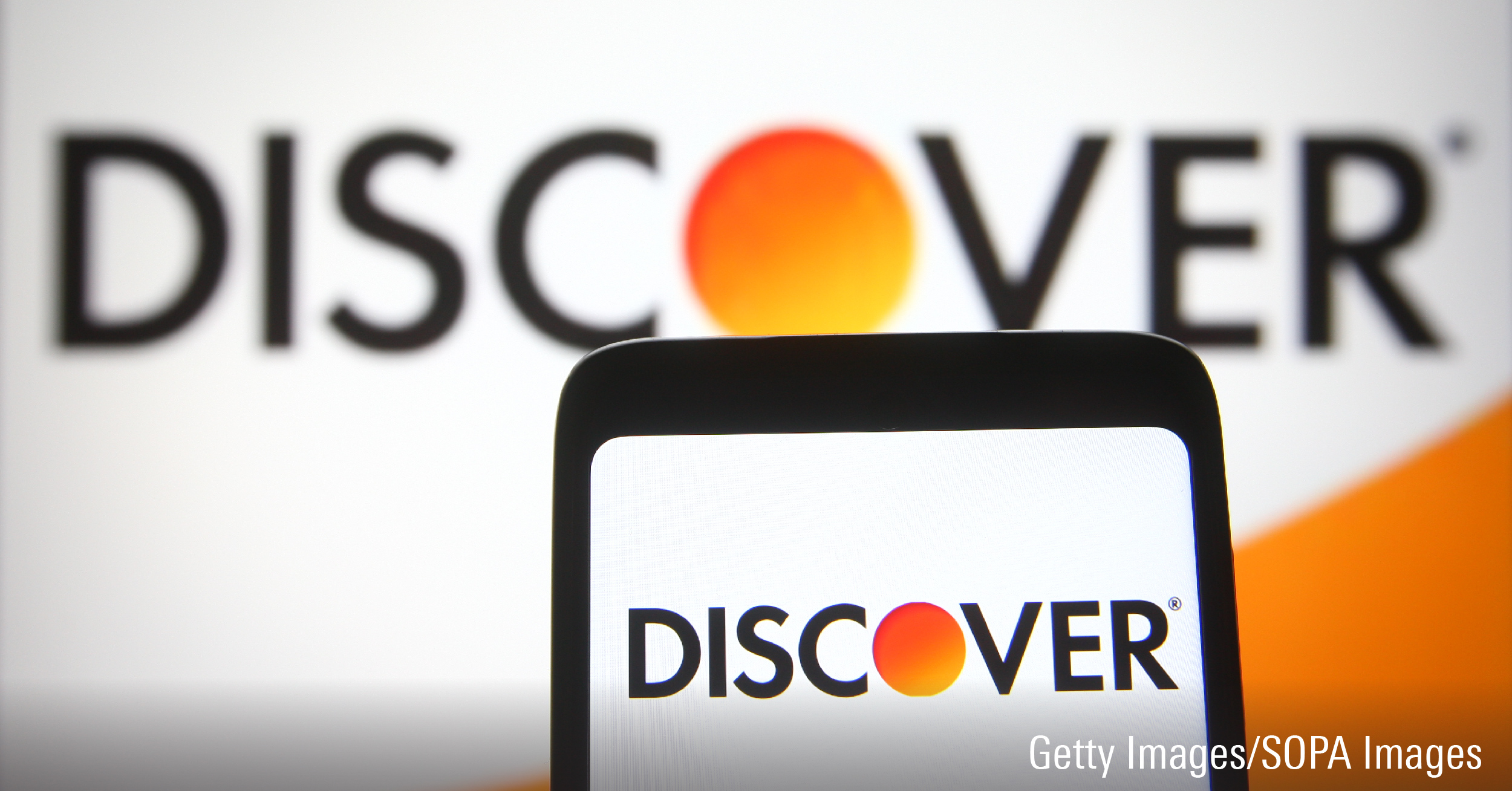 In this photo illustration a Discover logo of Discover Financial Services is seen on a smartphone and a pc screen.