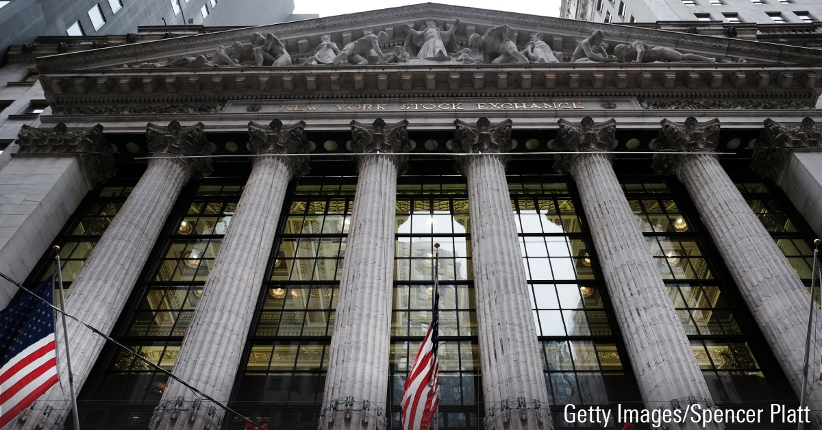 Photo looking up at the entrance to the New York Stock Exchange building. Columns and glass windows; American flags.