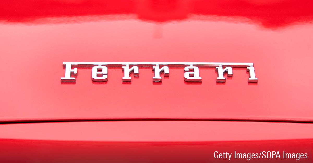 Ferrari logotype in silver appearing on a red hood of a vehicle.
