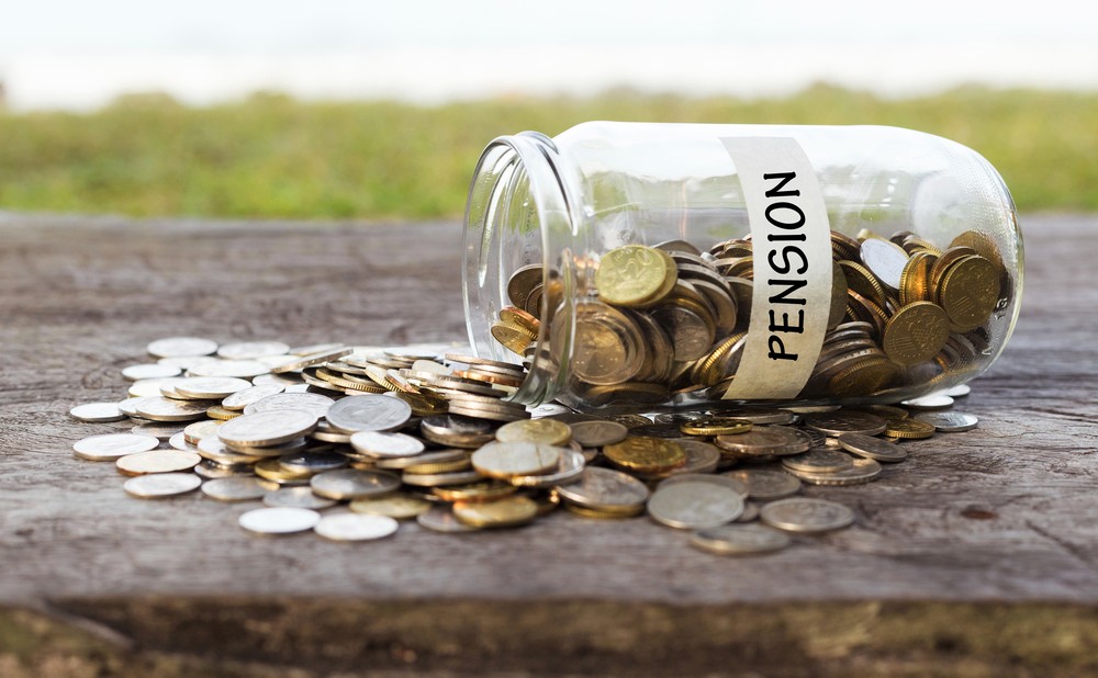 Coins in the jar or glass on the wood with PENSION label against bokeh beach background