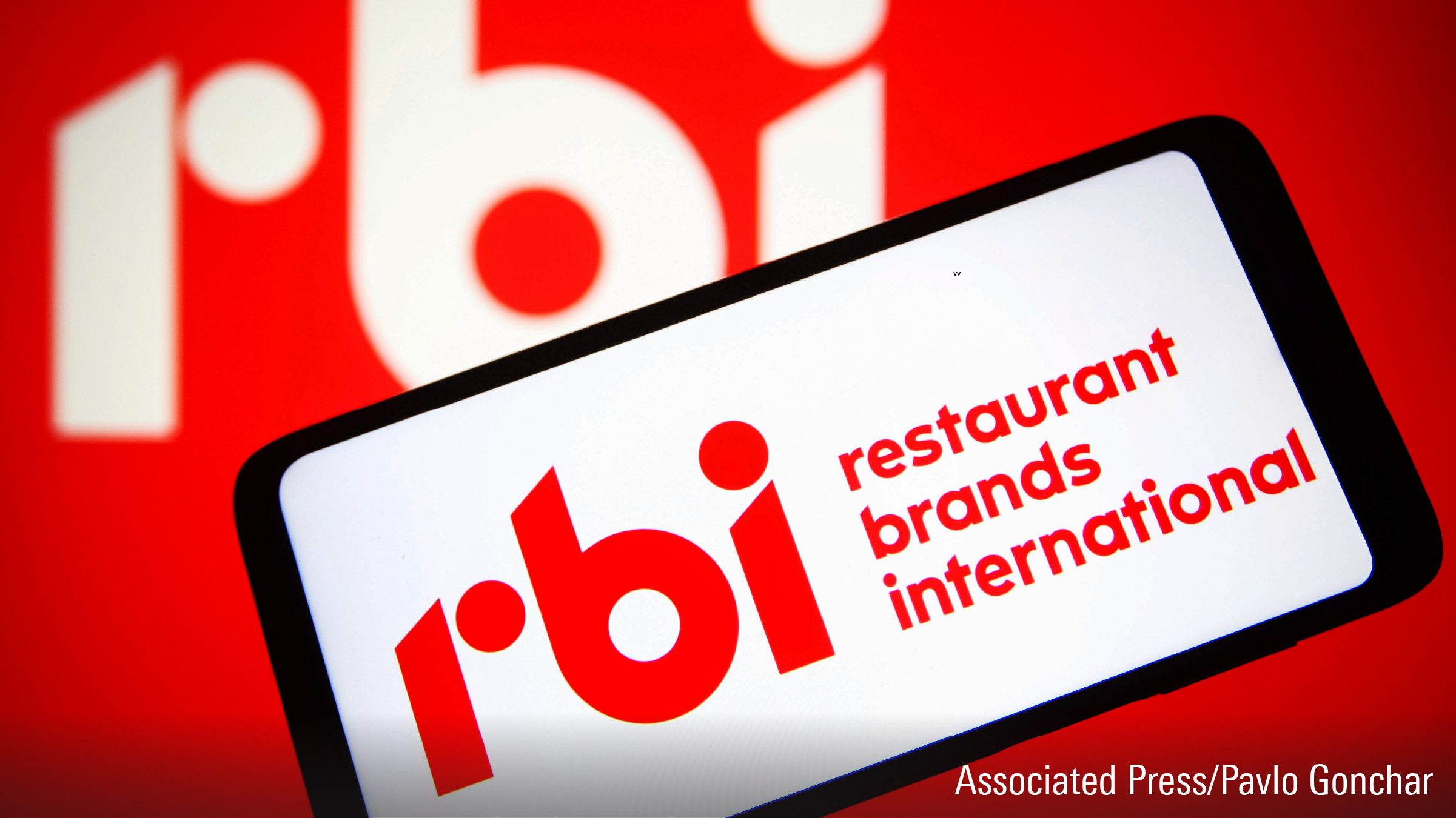 Un logo de Restaurant Brands International Inc. (RBI) est visible sur l'écran d'un smartphone et en arrière-plan.
