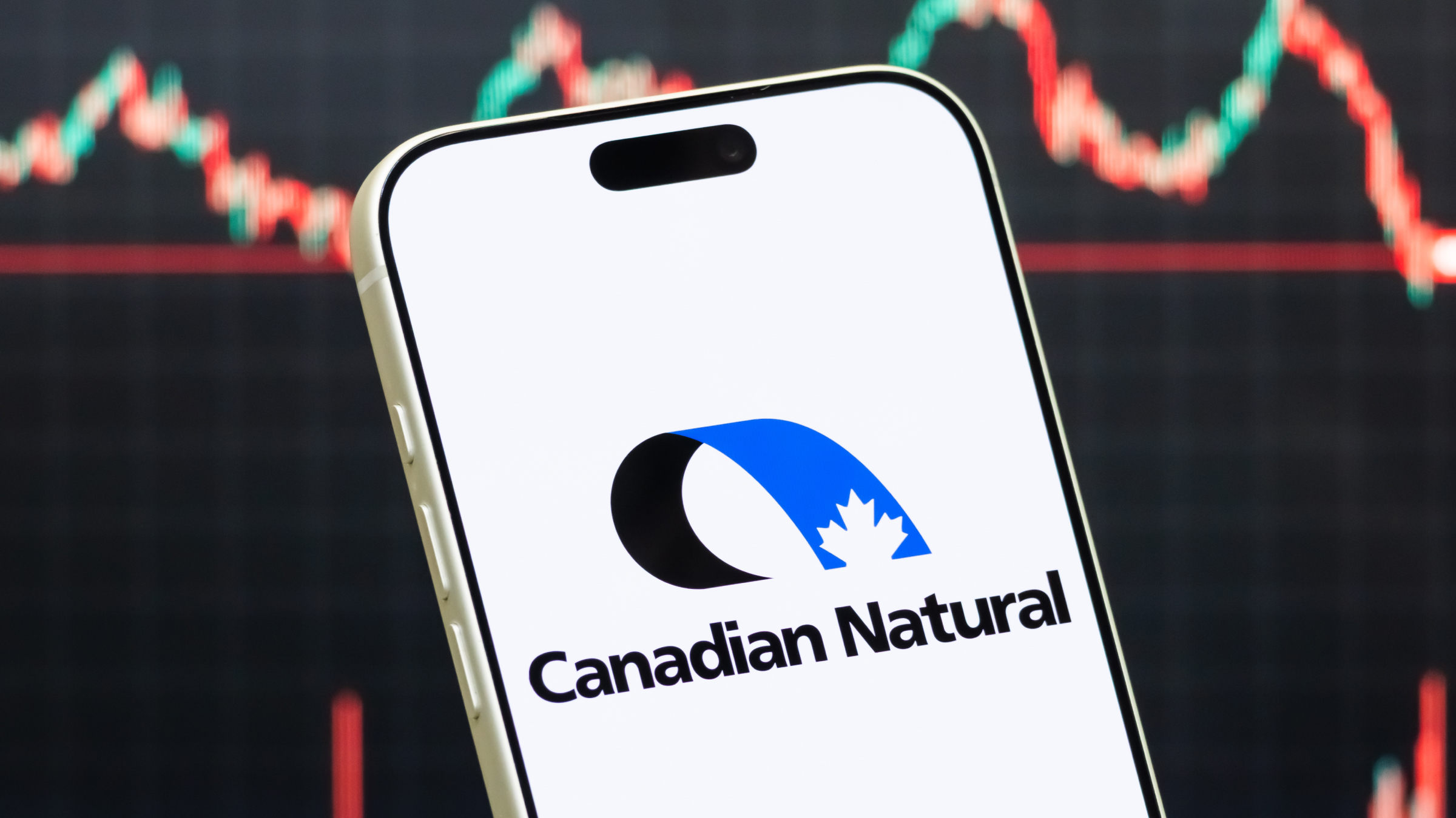 A smartphone displays the logo of Canadian Natural Resources Limited.