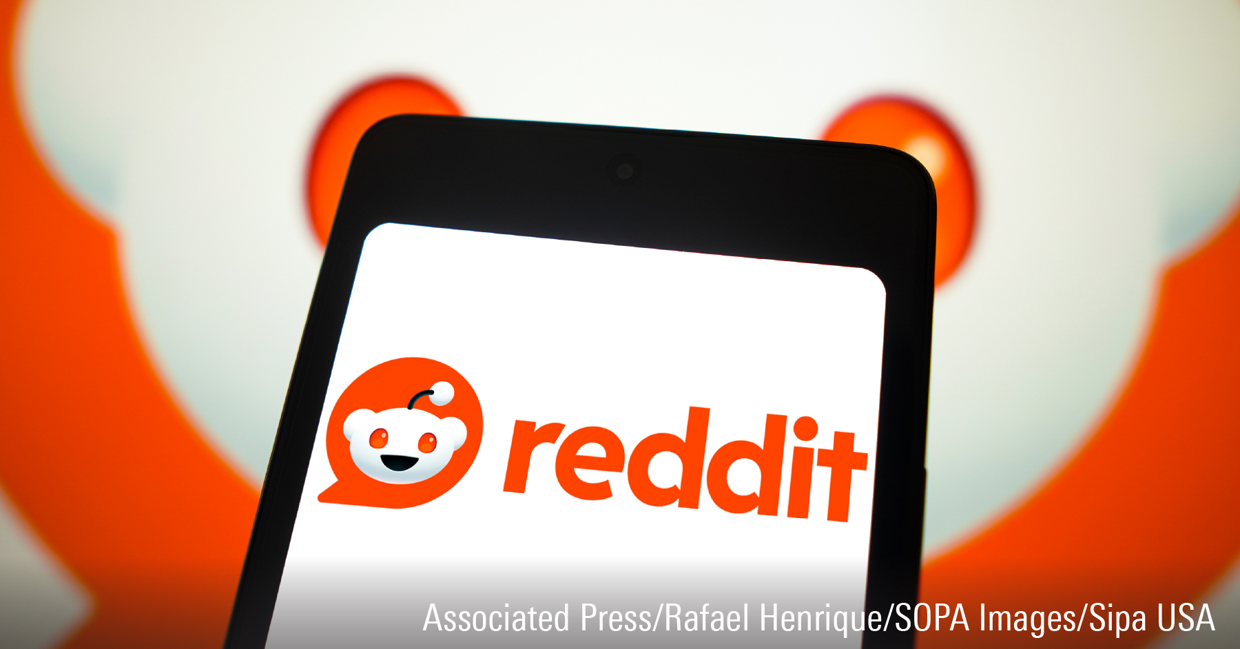 In this photo illustration, the Reddit logo is displayed on a smartphone screen and in the background.