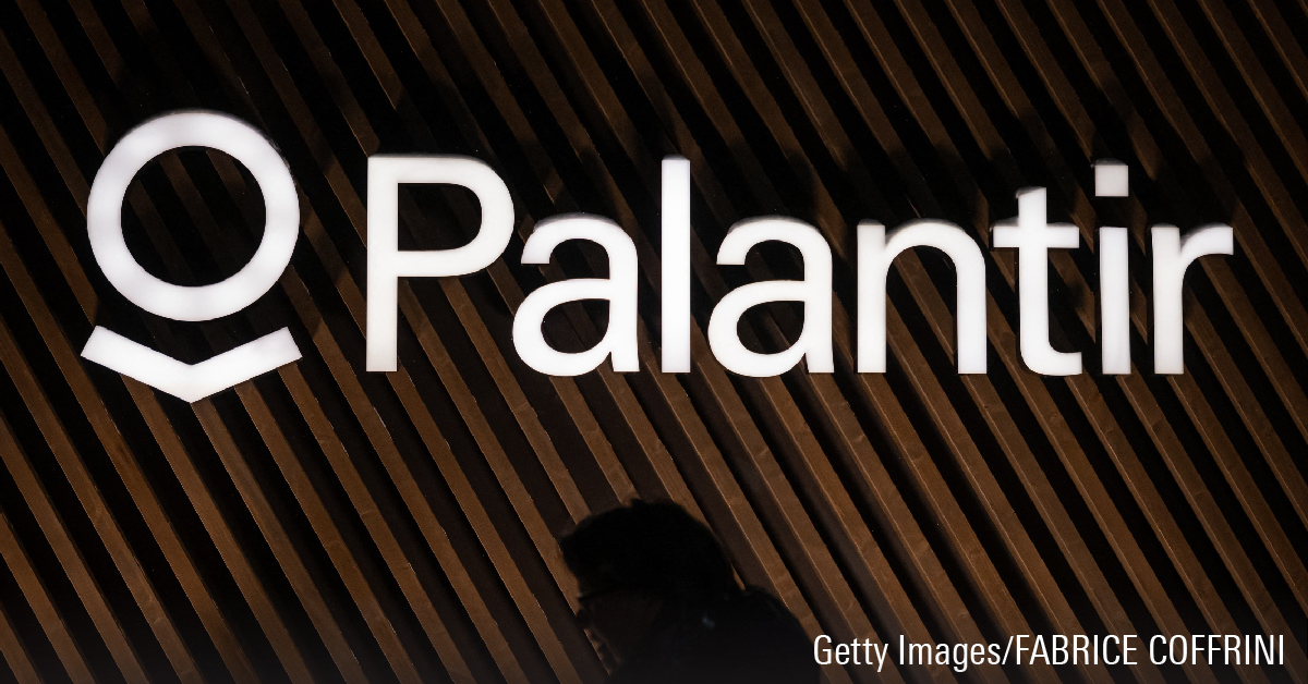 This photograph shows a woman walking past the logo of Palantir Technologies during the World Economic Forum.