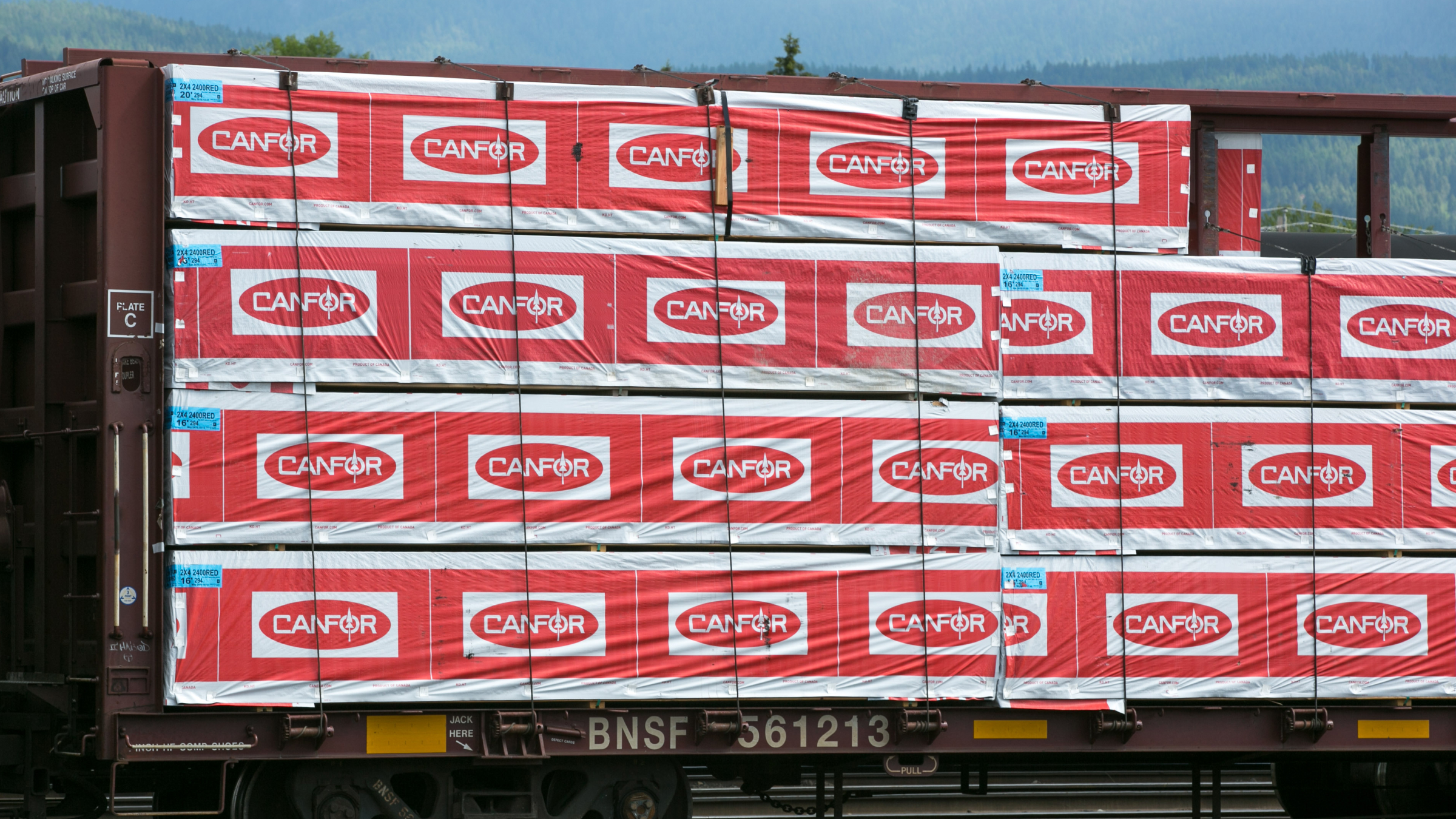 Freight train hauling finished wood and lumber products with the Canfor logo.