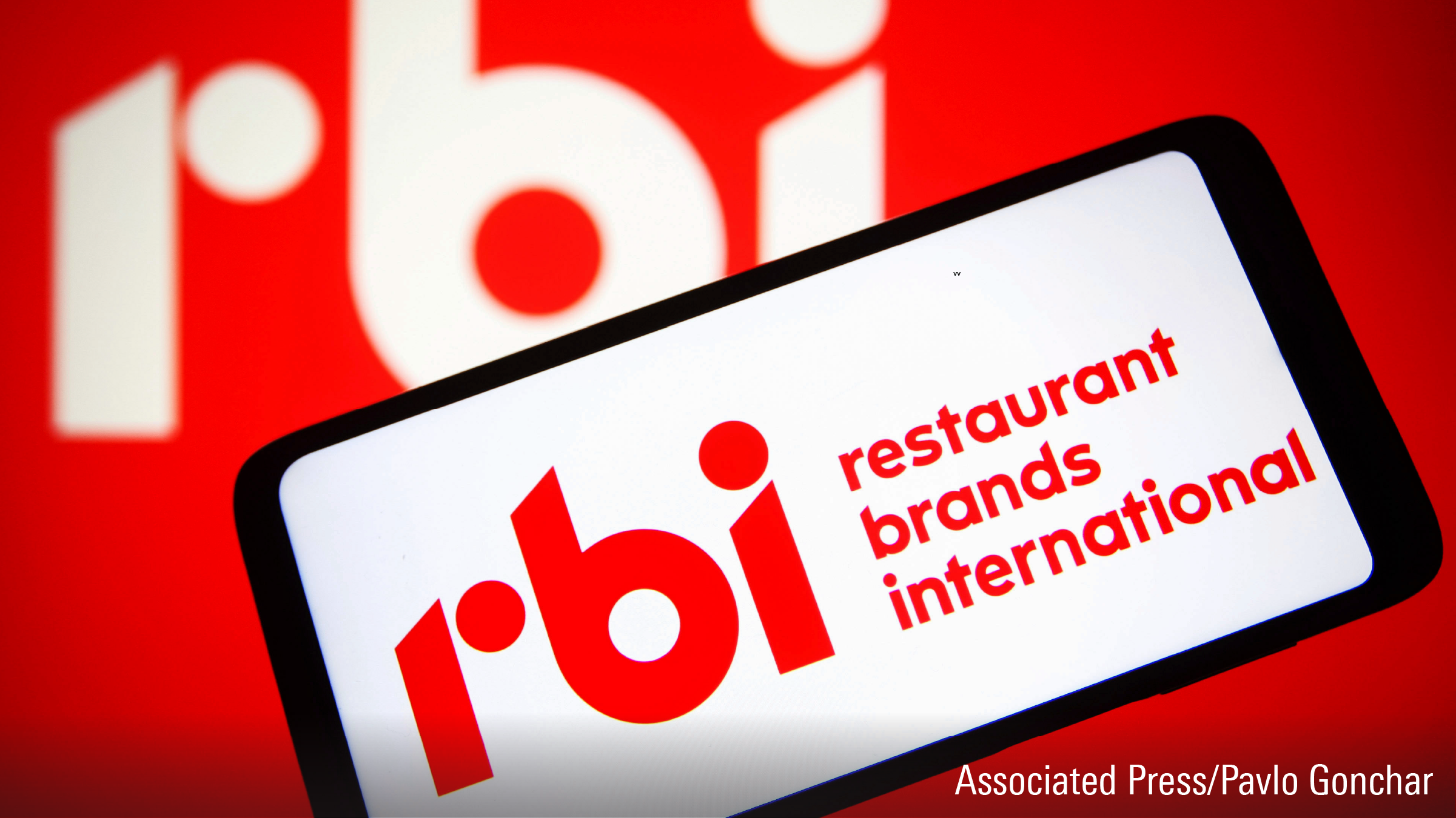 A Restaurant Brands International Inc. (RBI) logo is seen on a smartphone screen and in the background.