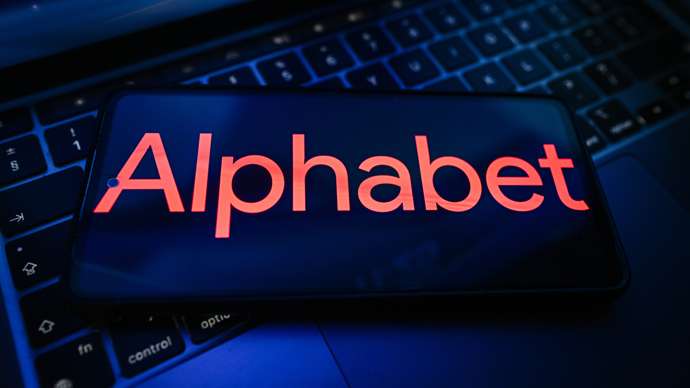 An Alphabet logo displayed on a smartphone on the top of a laptop.