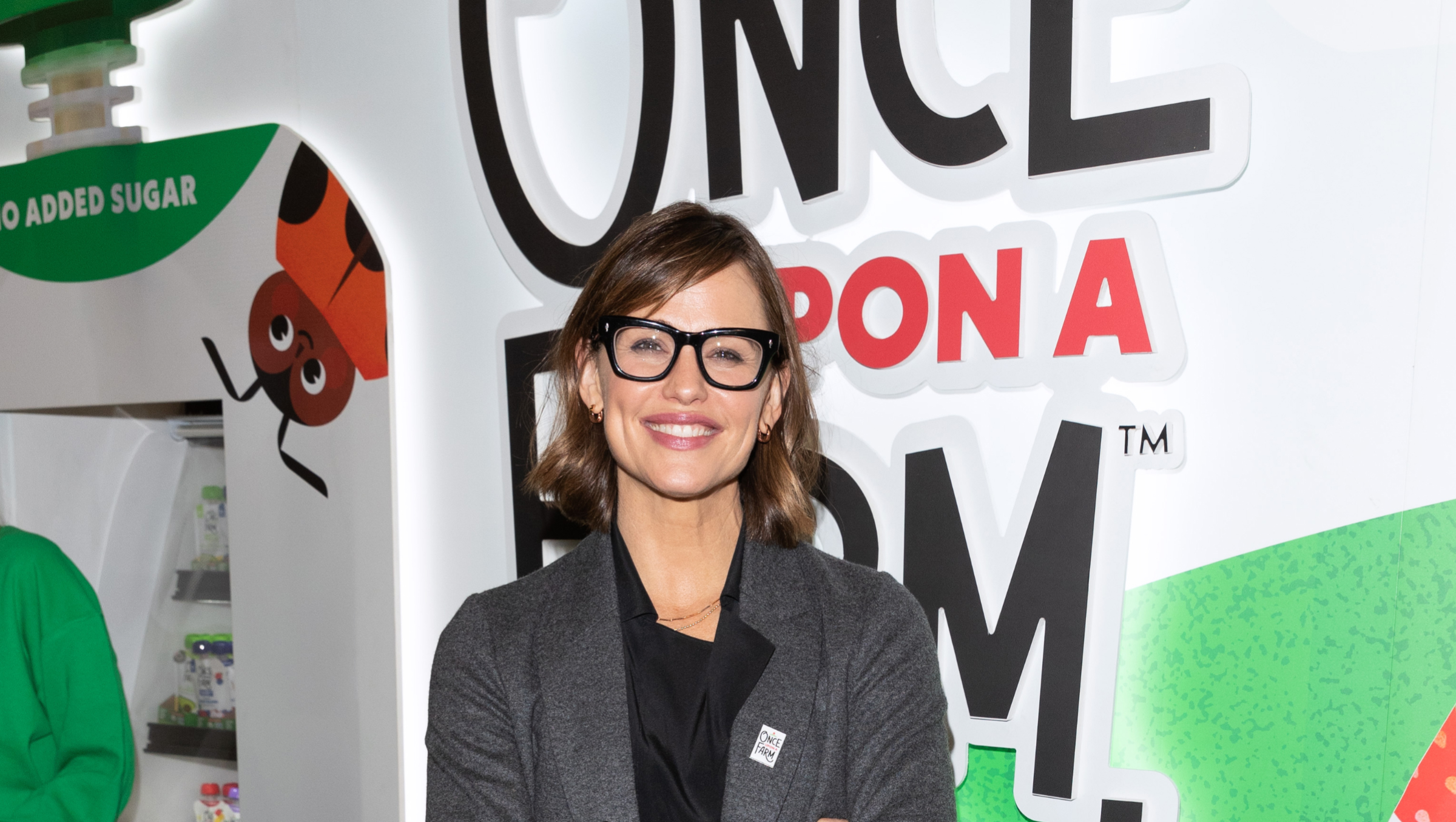 Jennifer Garner stands in front of a "Once Upon A Farm" stand at a convention.