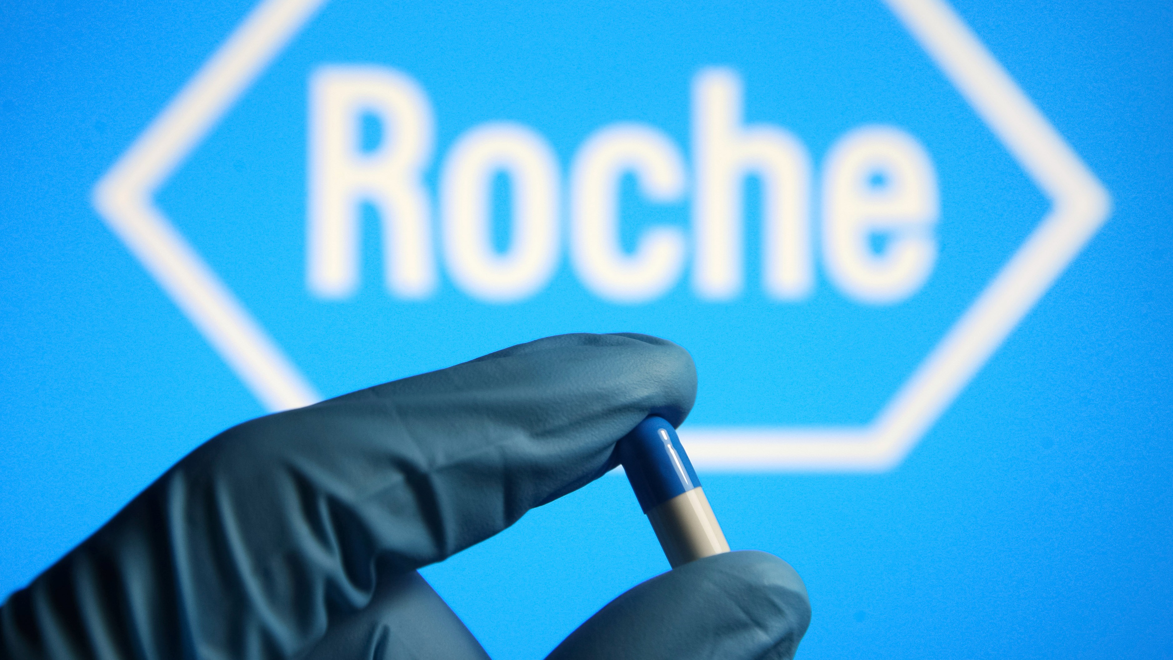 In this photo illustration, a medicine pill in form of a capsule is seen in a hand dressed in a medical glove with a Roche Holding AG logo of a pharmaceutical company in the background. (Photo by Pavlo Gonchar / SOPA Images/Sipa USA)(Sipa via AP Images)