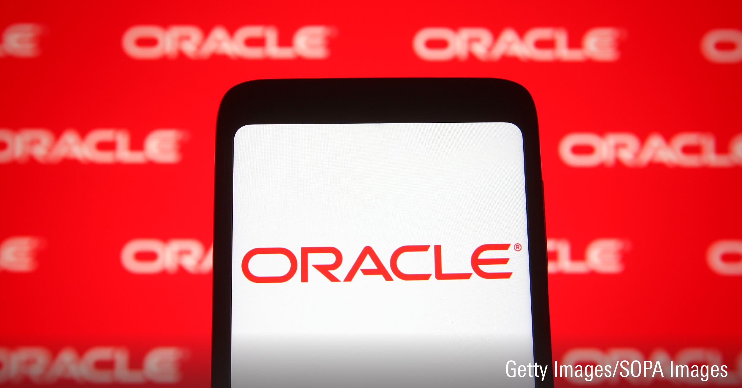 In this photo illustration an Oracle logo is seen on a smartphone and a pc screen.