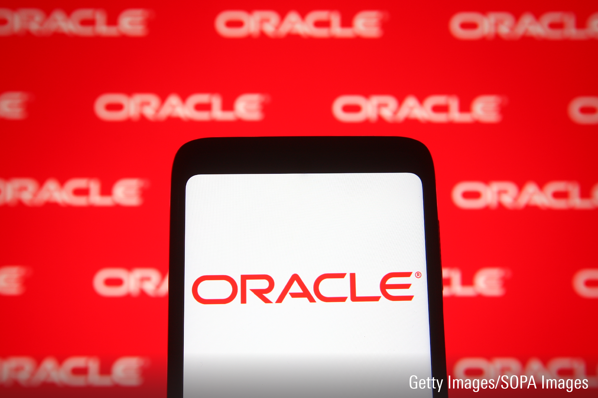 In this photo illustration an Oracle logo is seen on a smartphone and a pc screen.