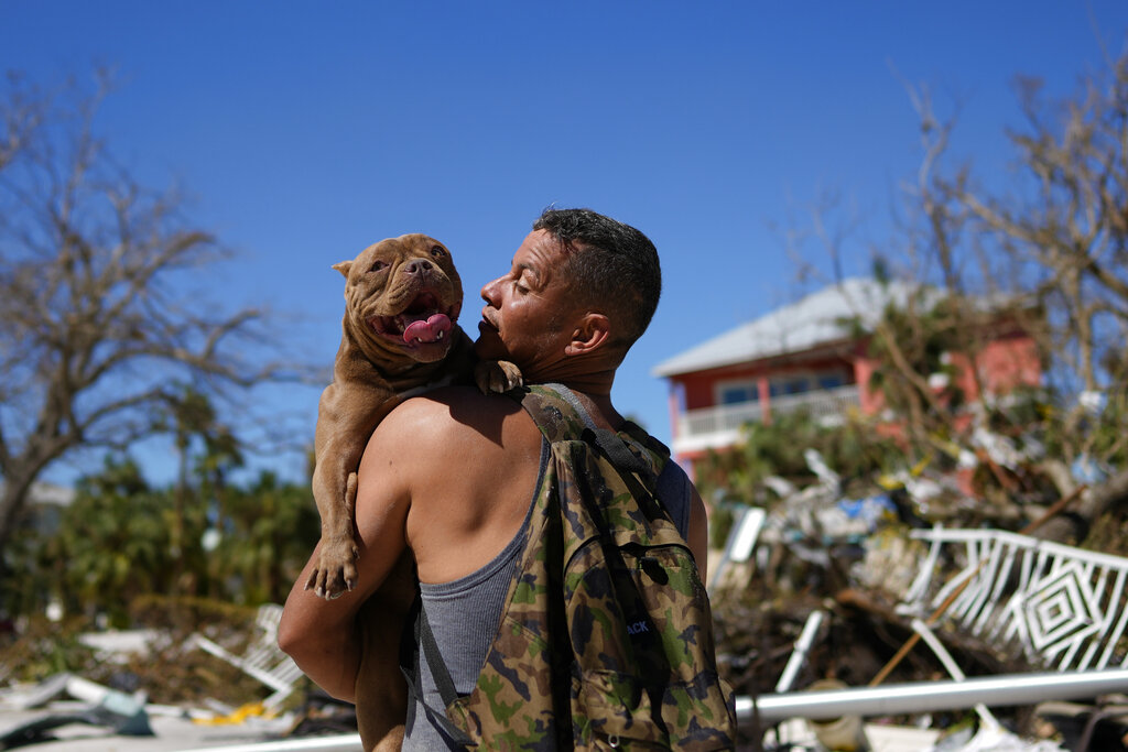 A man carries a dog he recovered in hopes of reuniting it with its owners, two days after the passage of Hurricane Ian, in Fort Myers Beach, Fla., Friday, Sept. 30, 2022.